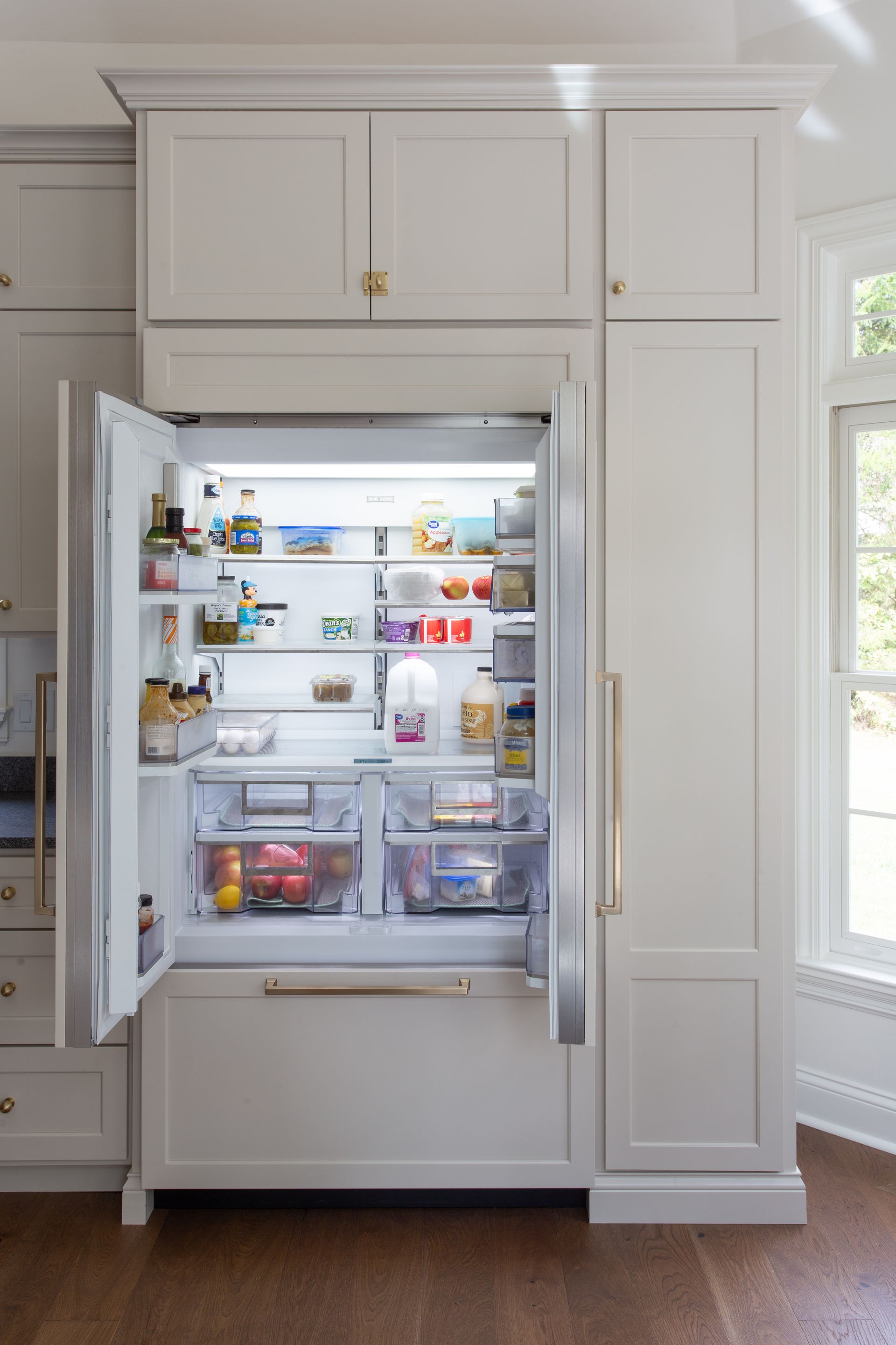 White kitchen refrigerator with doors open, showcasing groceries.