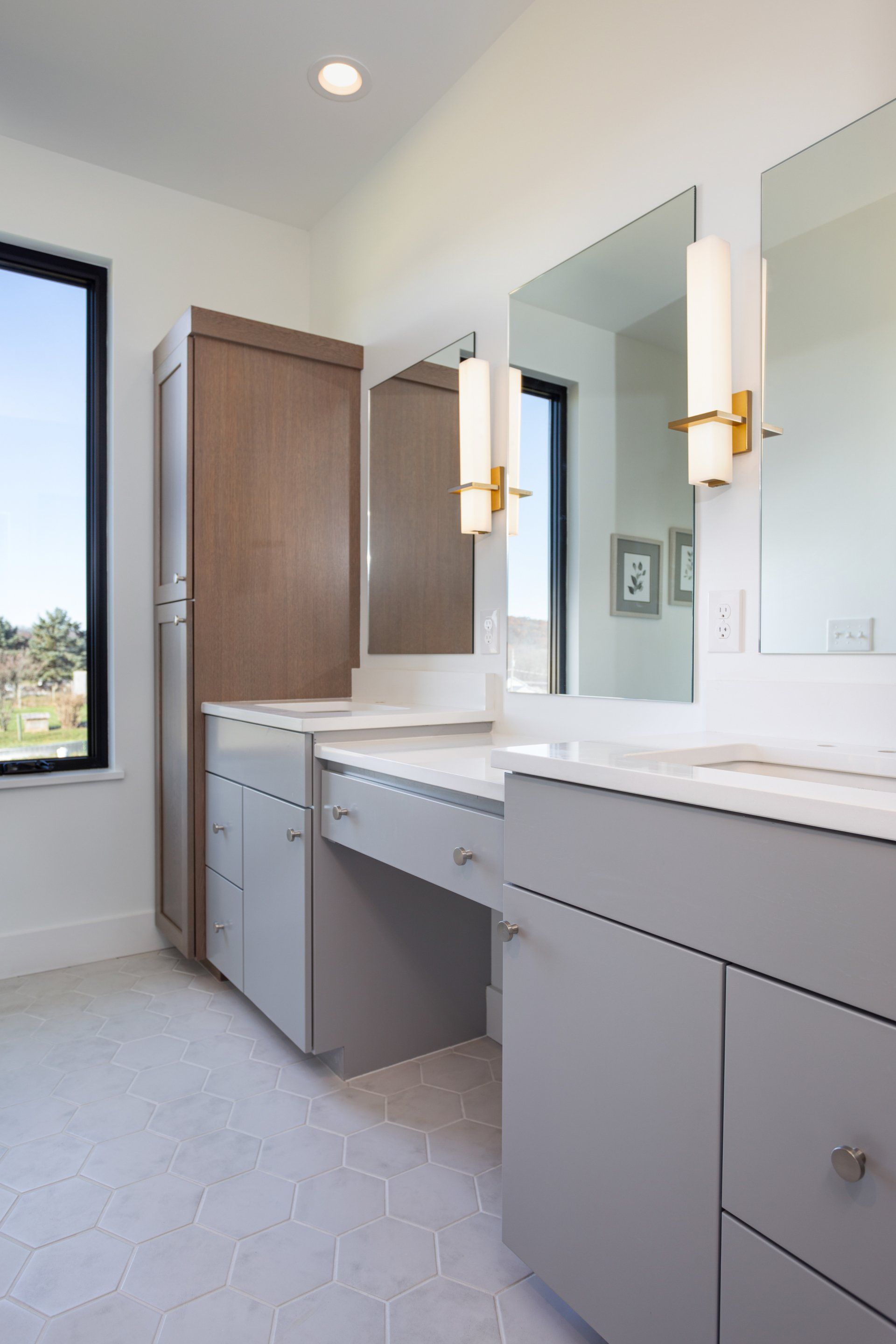 Bathroom with gray vanity, mirrors, and a tall cabinet, with a large window and white tile floor.