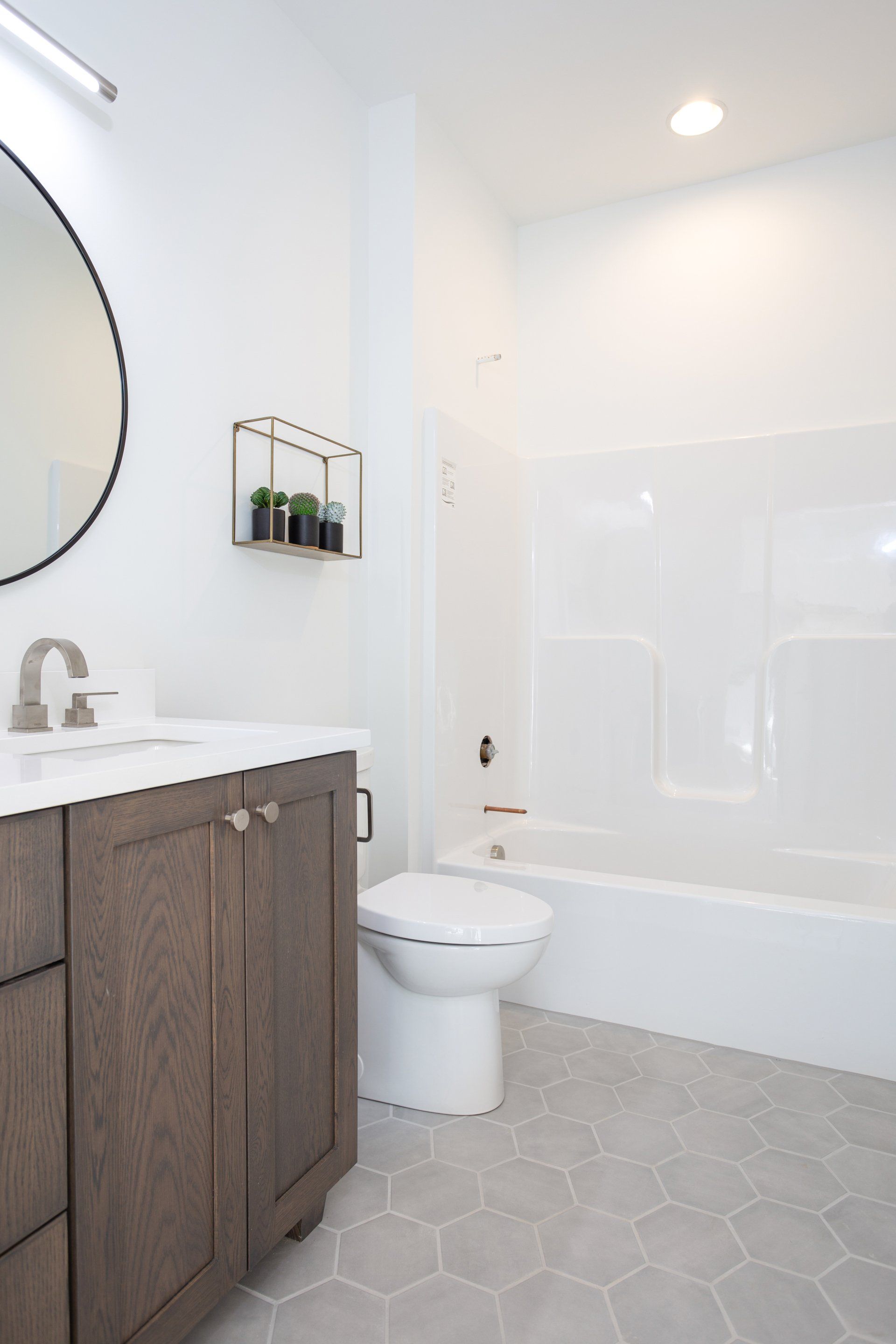 Bathroom with a wood vanity, white toilet, and gray hexagonal floor tiles.