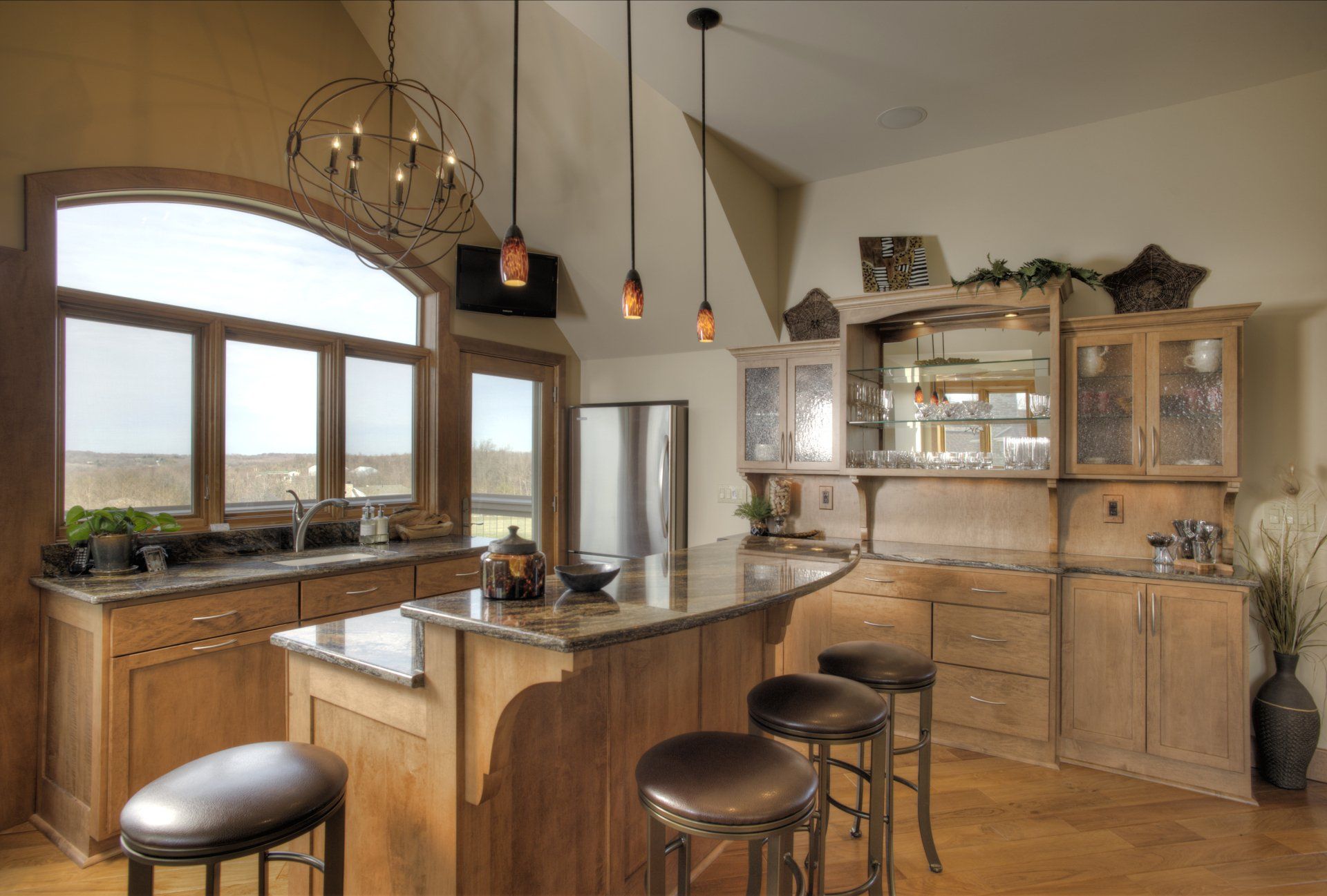 Kitchen with wooden cabinets, island with stools, and large arched window.