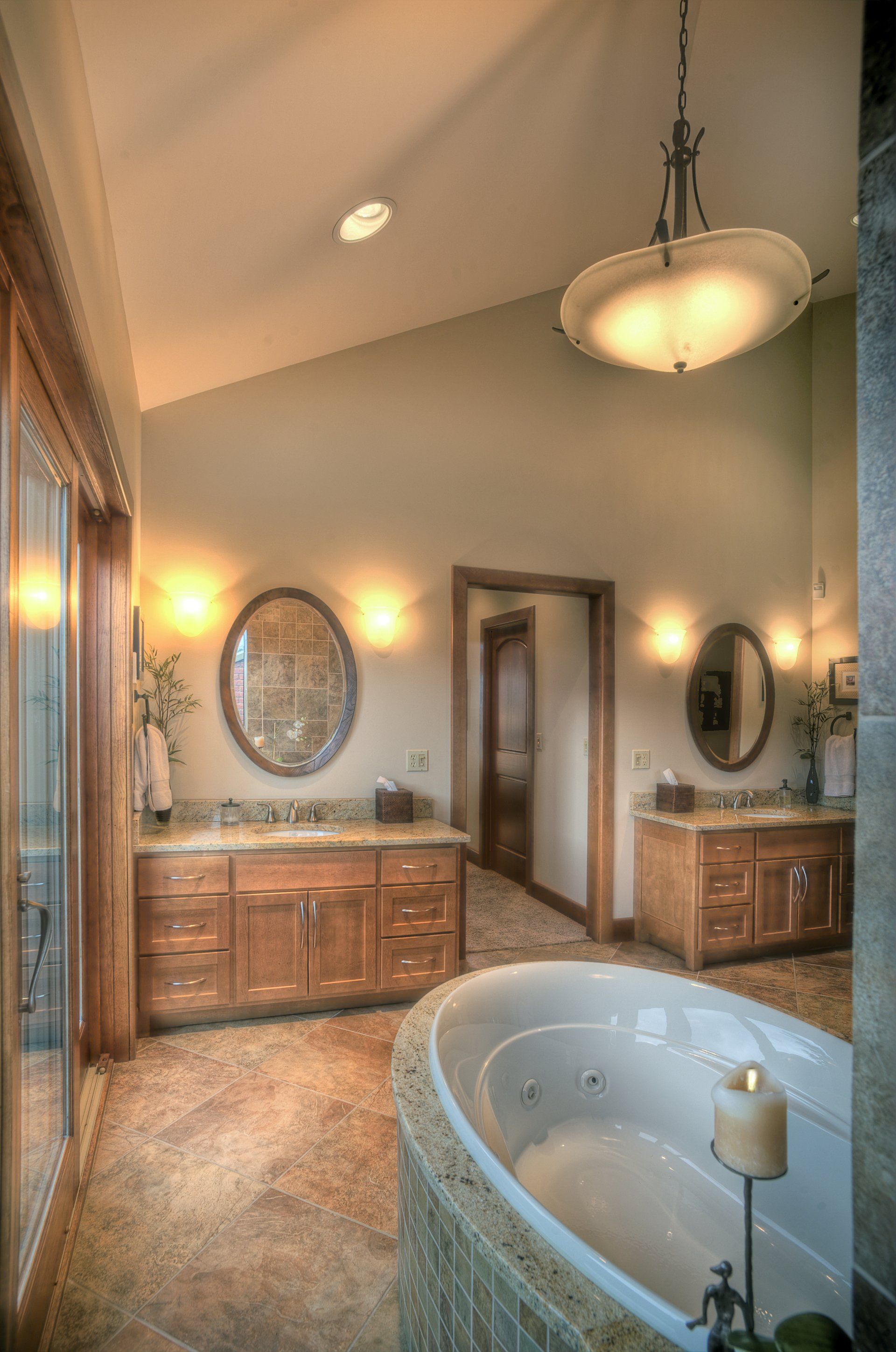 Spacious bathroom with oval tub, double vanity, pendant light, and large mirrors. Light wood and stone details.