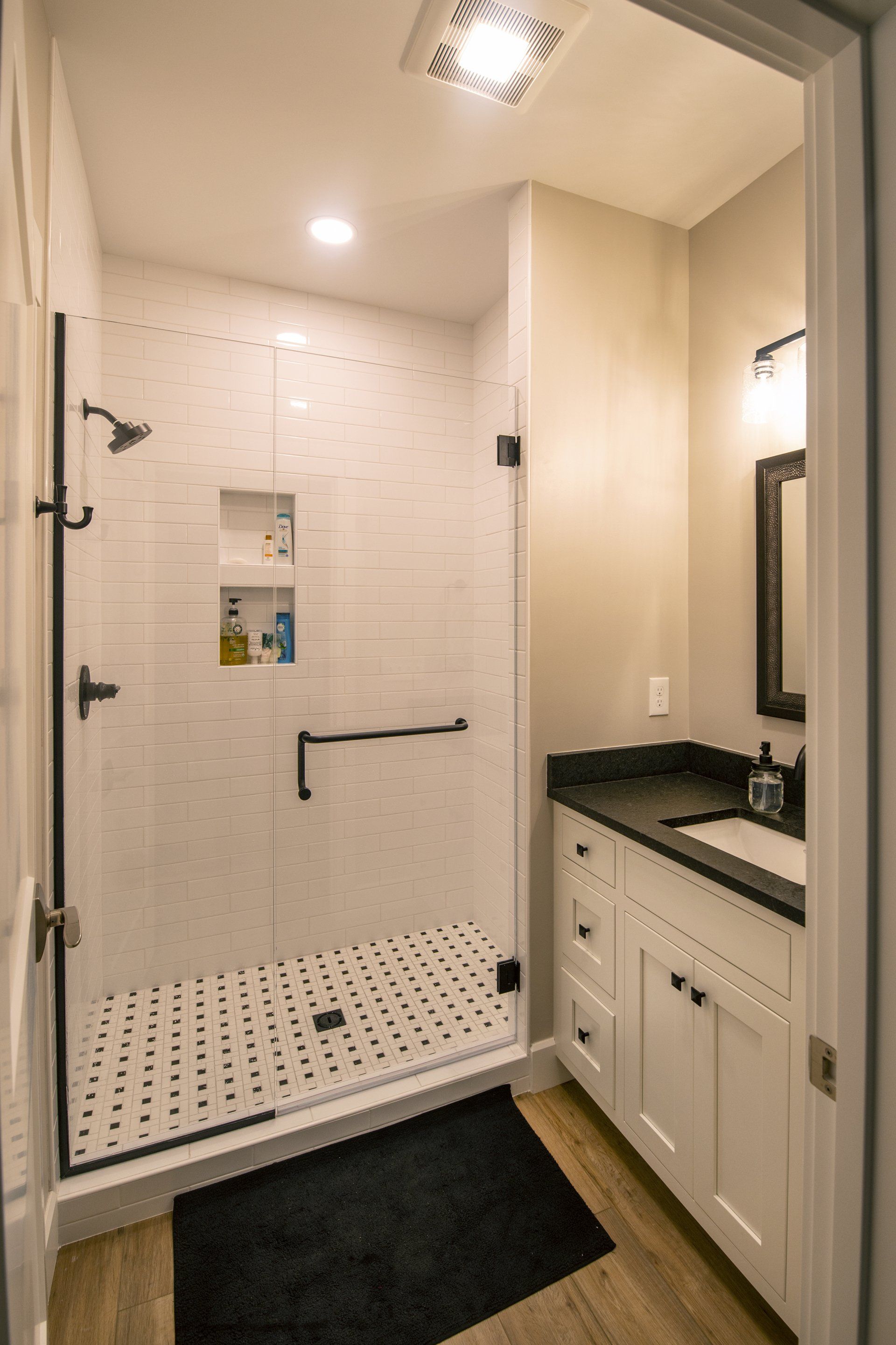 Modern bathroom with white subway tile shower, black fixtures, and a white vanity with black countertop.