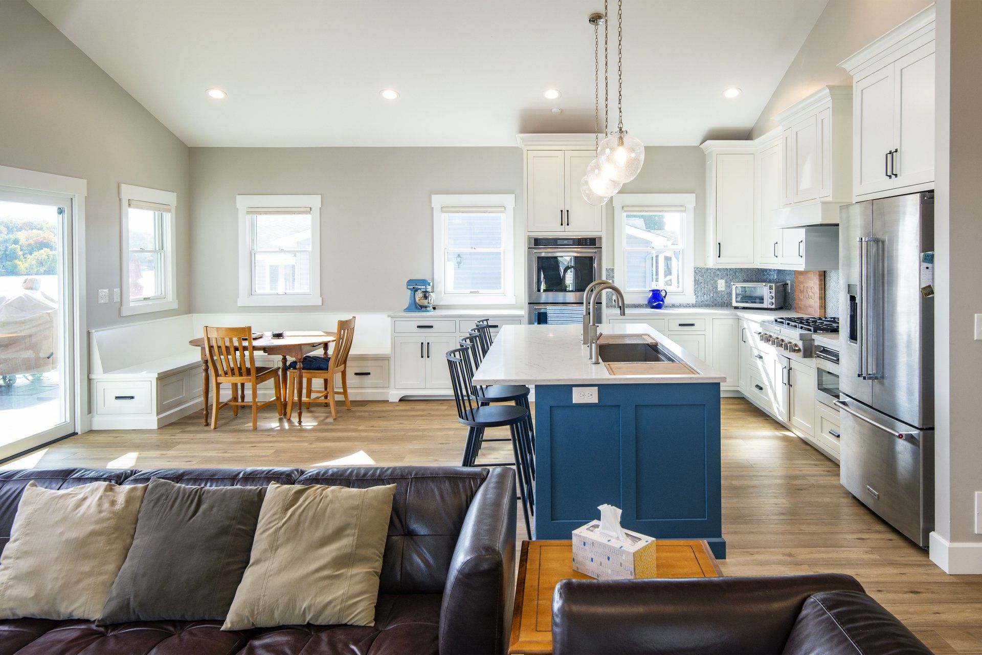 Open-concept kitchen with white cabinets, blue island, stainless steel appliances, and a dining area.