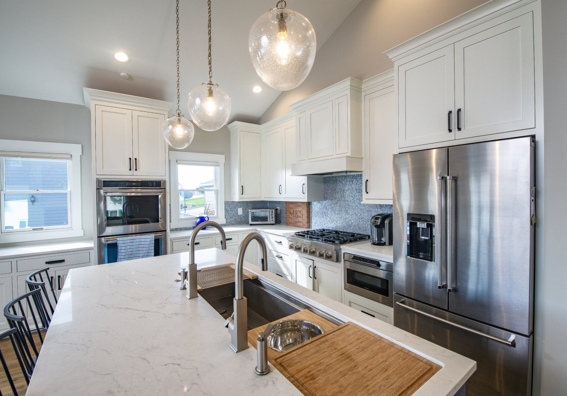 Bright white kitchen with stainless steel appliances, marble countertops, and pendant lights.