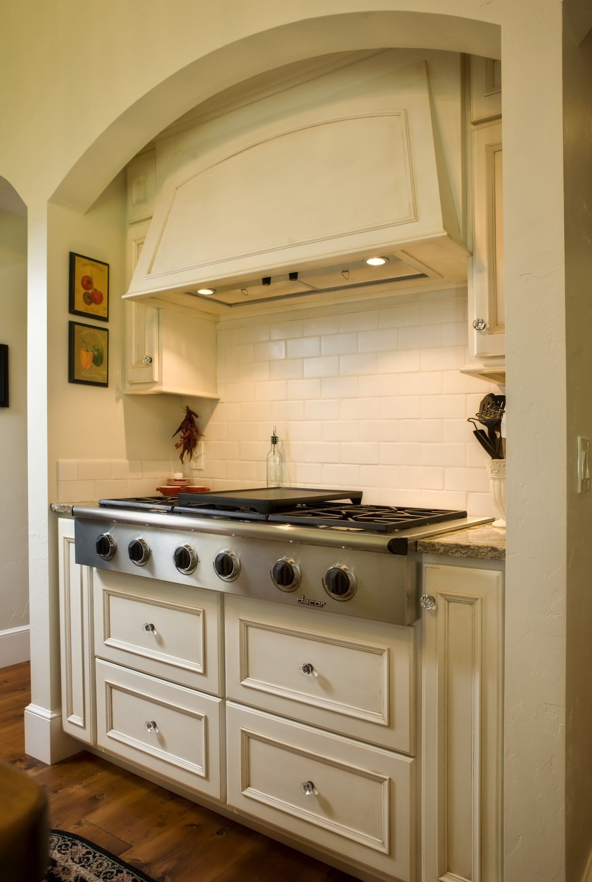 Cream-colored kitchen stove and range hood, white subway tile backsplash, drawers.