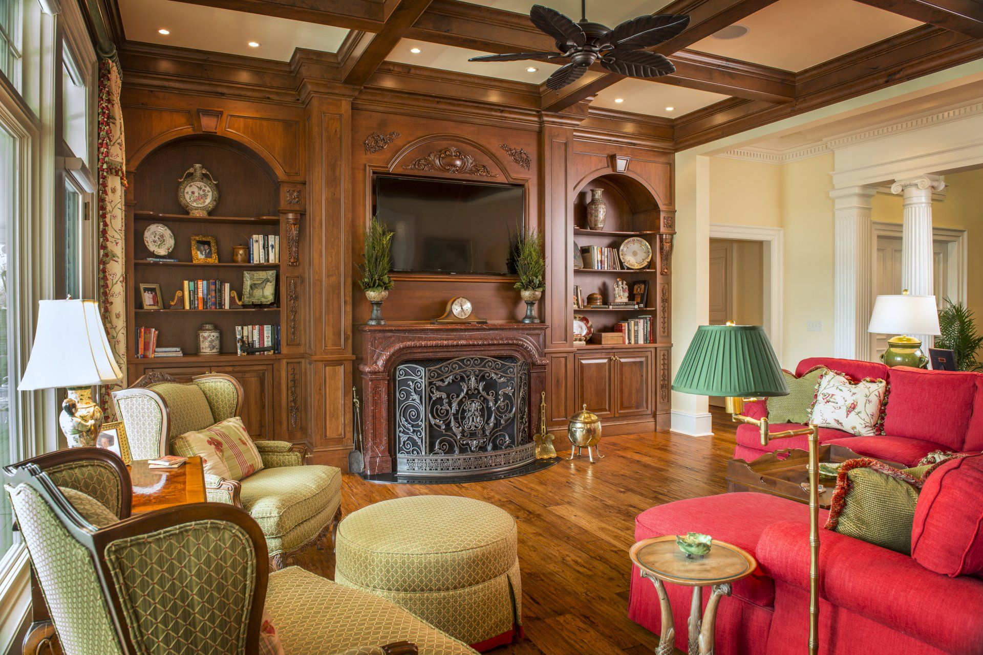 Luxurious living room with wooden built-ins, red sofa, green armchairs, and a fireplace.