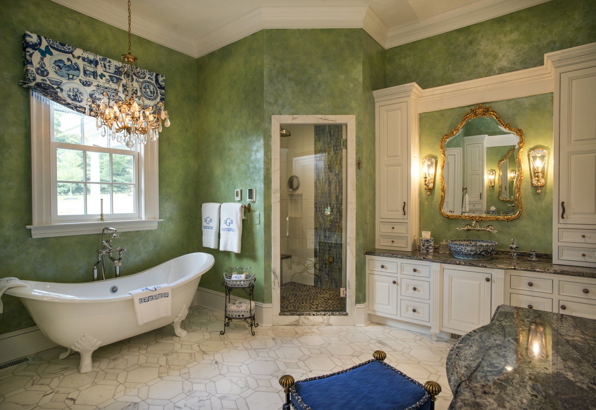 Luxurious green bathroom with white clawfoot tub, gold-framed mirror, and chandelier.