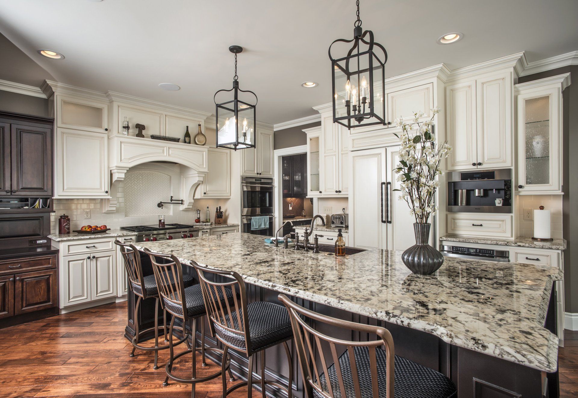 Kitchen with large granite island, white cabinets, dark stools, and two black pendant lights.