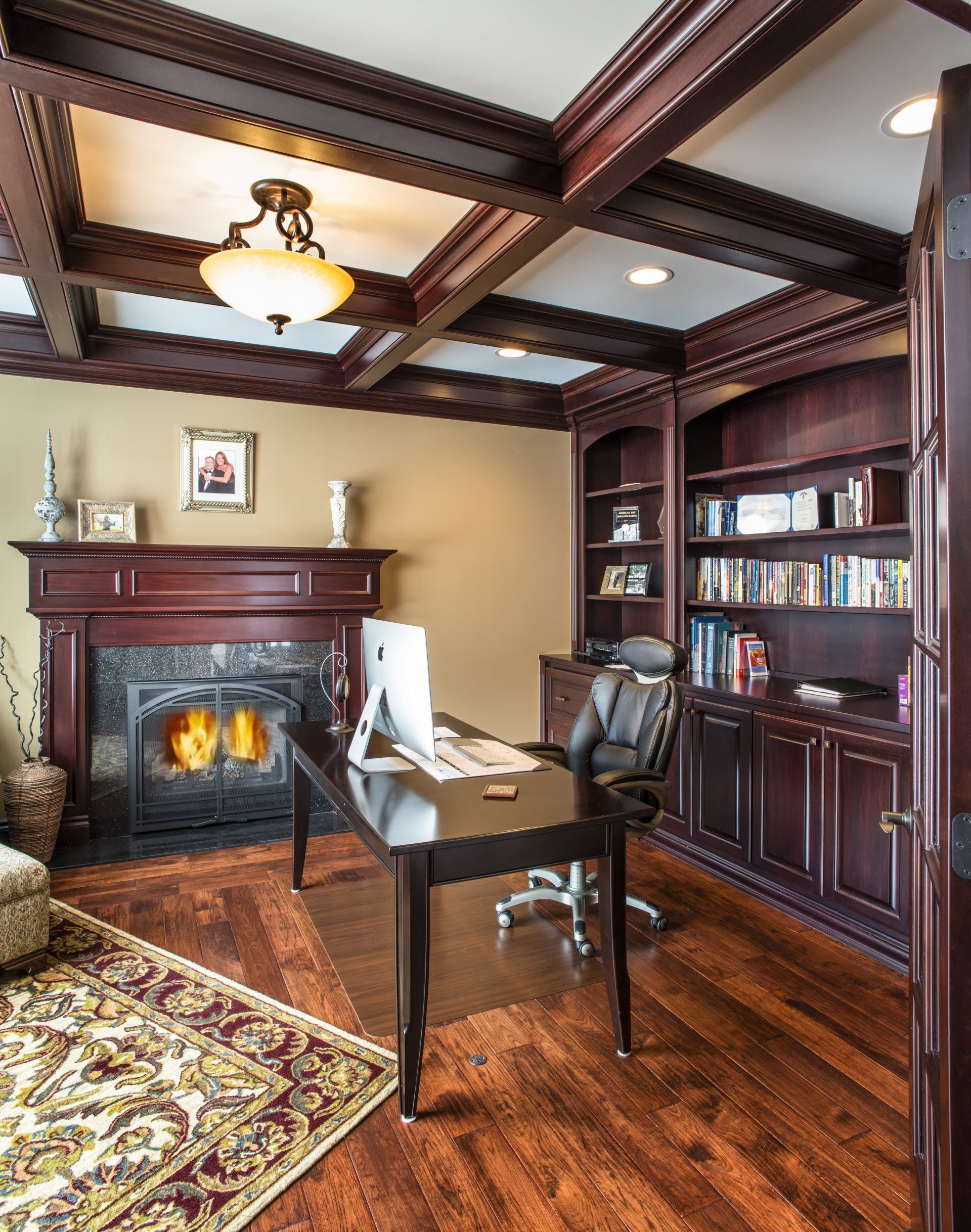 Elegant home office with dark wood paneling, fireplace, built-in bookshelves, and a desk.