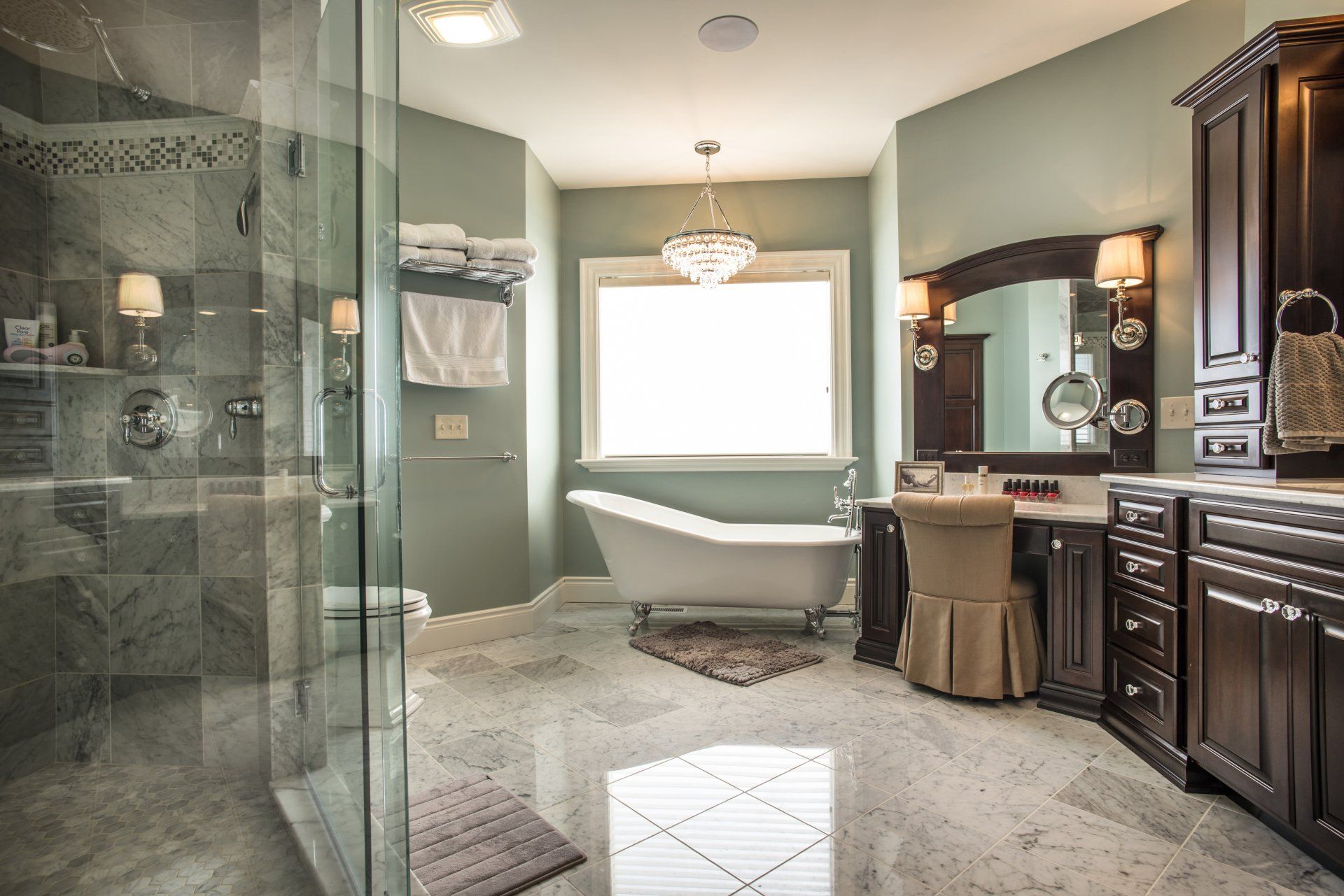 Luxurious bathroom with clawfoot tub, marble floor, glass shower, vanity, and dark wood cabinets.