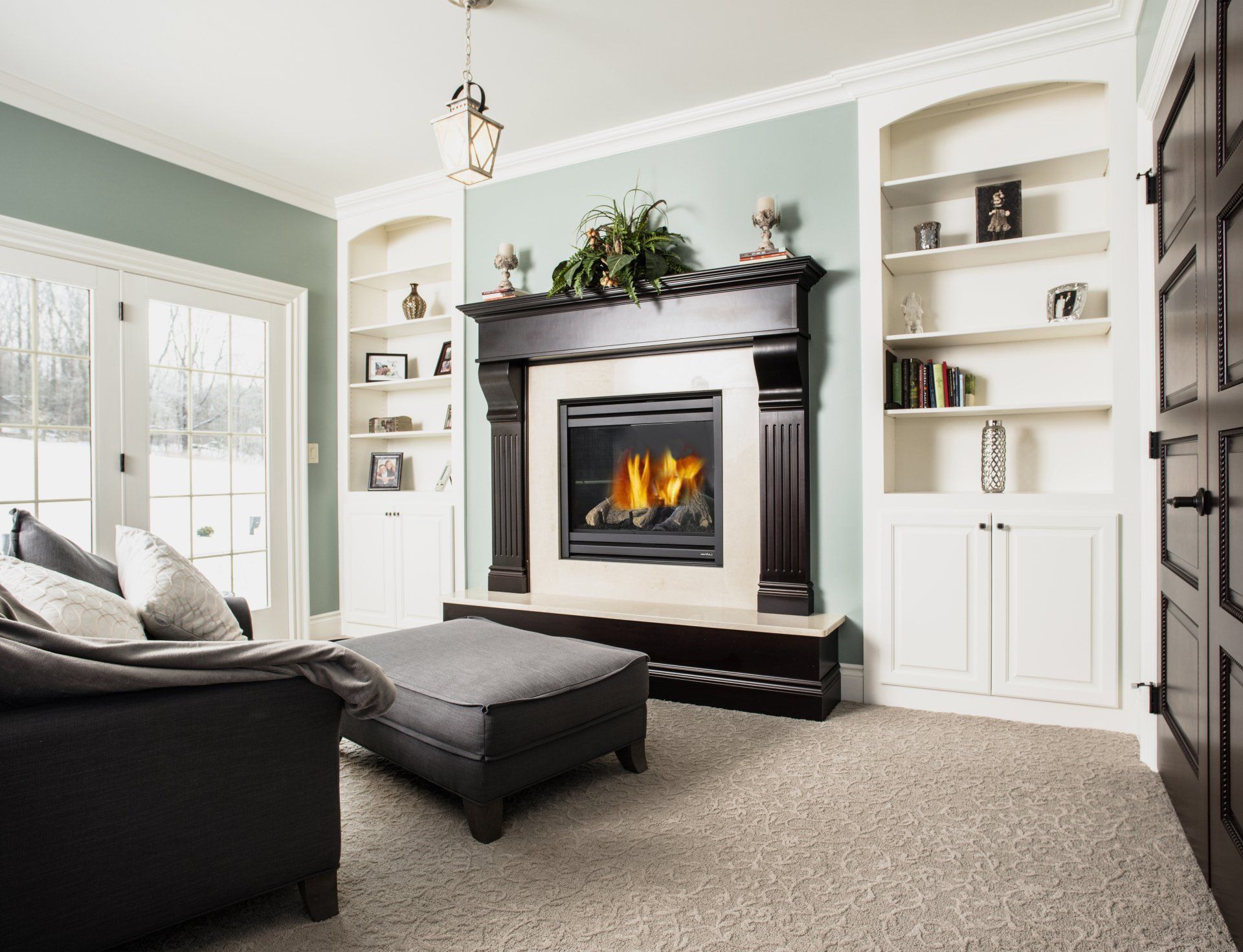 Living room with fireplace, built-in shelves, sofa, and ottoman. Soft green walls and neutral carpet.