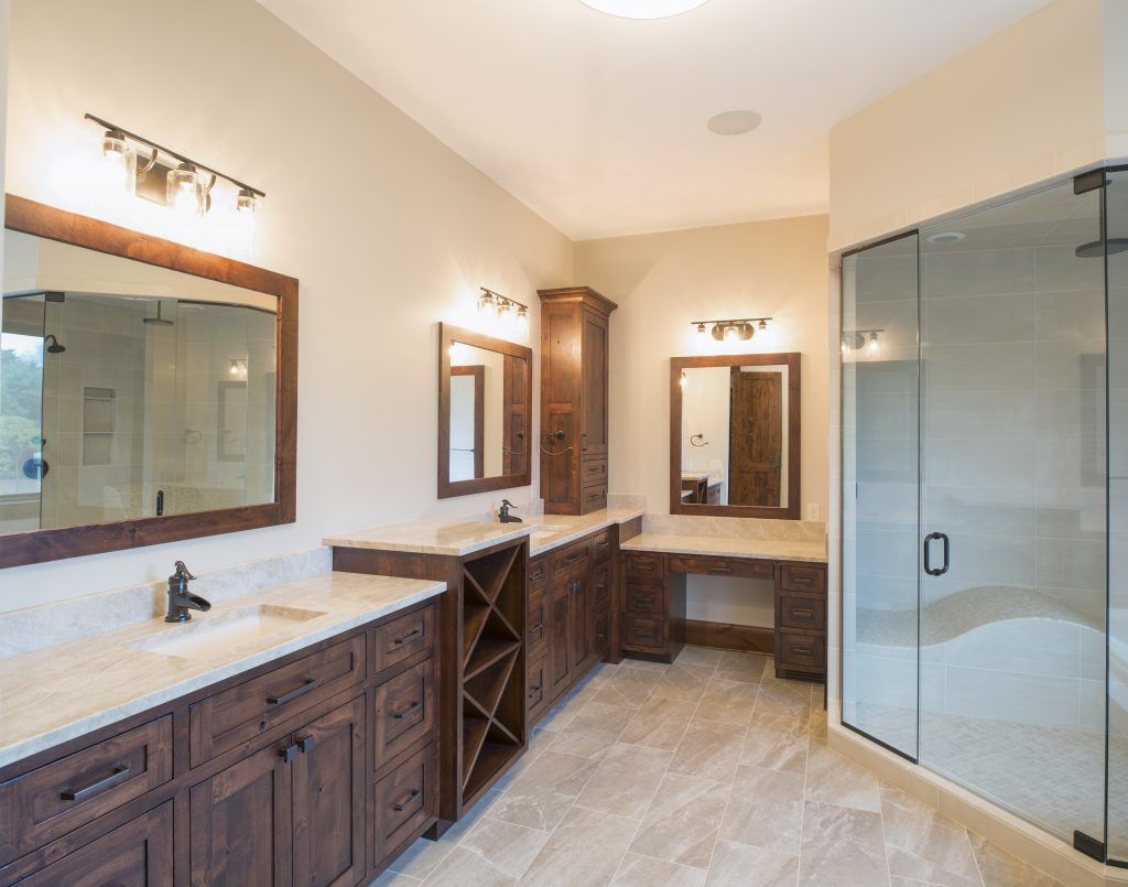 Spacious bathroom with dark wood vanities, light countertops, large mirrors, and a glass shower.