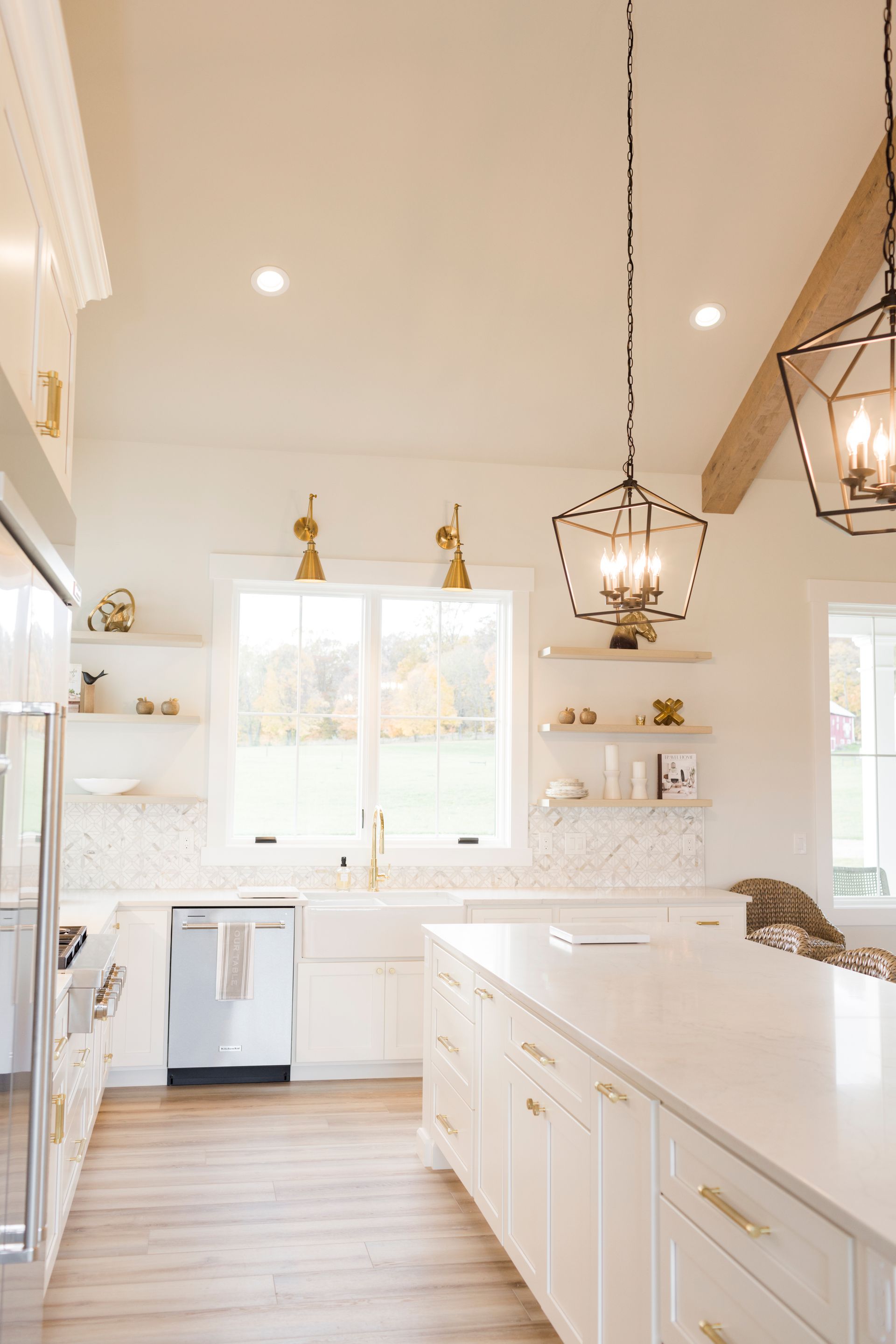 Bright, modern kitchen with white cabinets, gold hardware, island, open shelves, and geometric light fixtures.