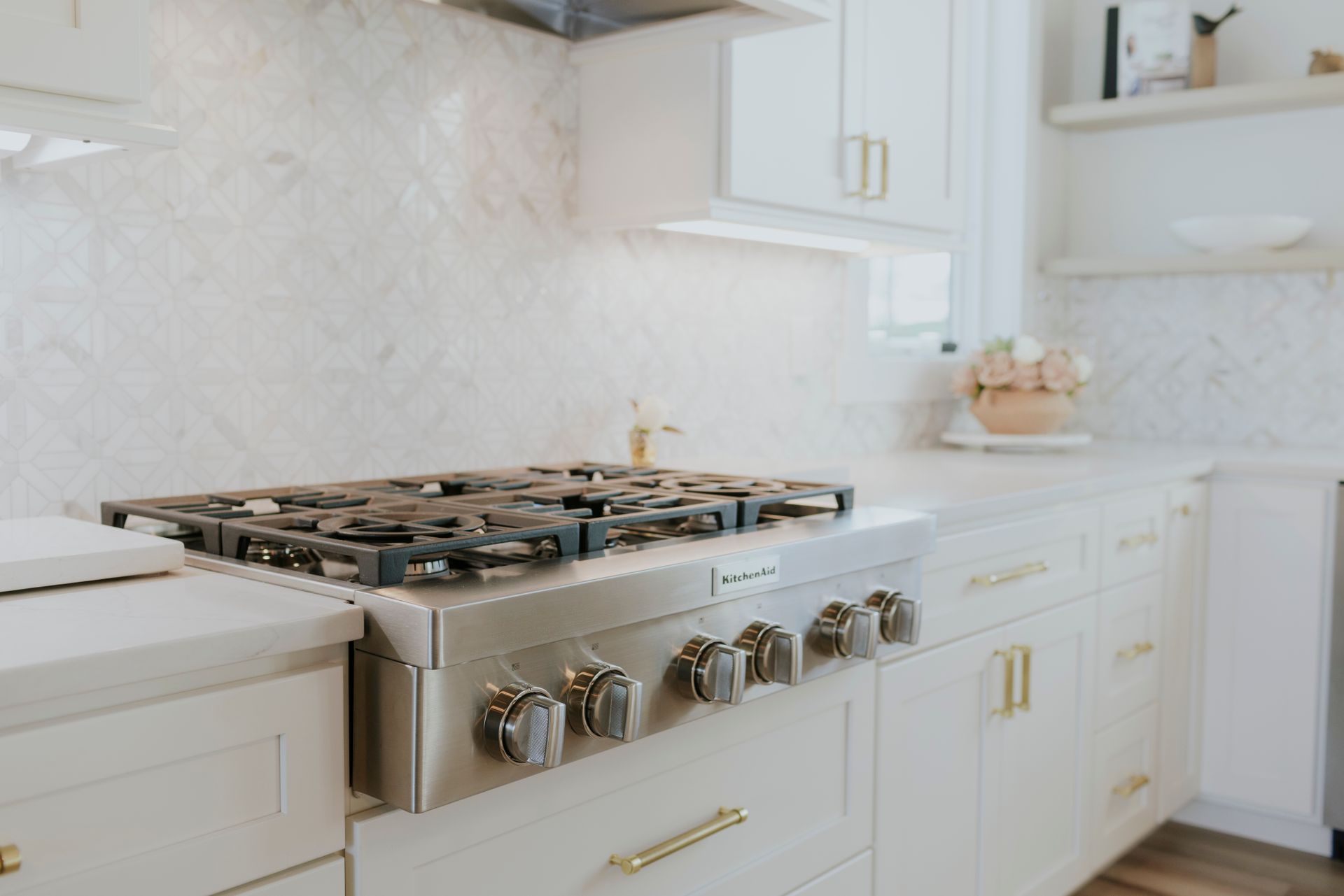 Modern white kitchen with stainless steel range and gold hardware.