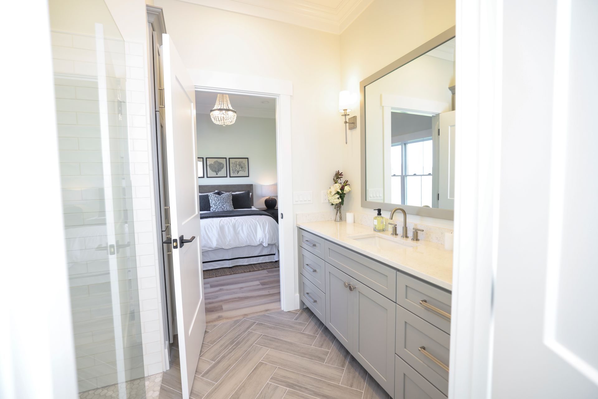 Bathroom with gray vanity, large mirror, and view into bedroom with a bed.