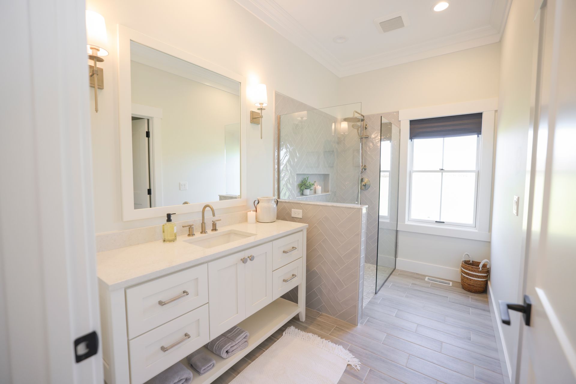 White bathroom with vanity, shower, window, and neutral color tile.