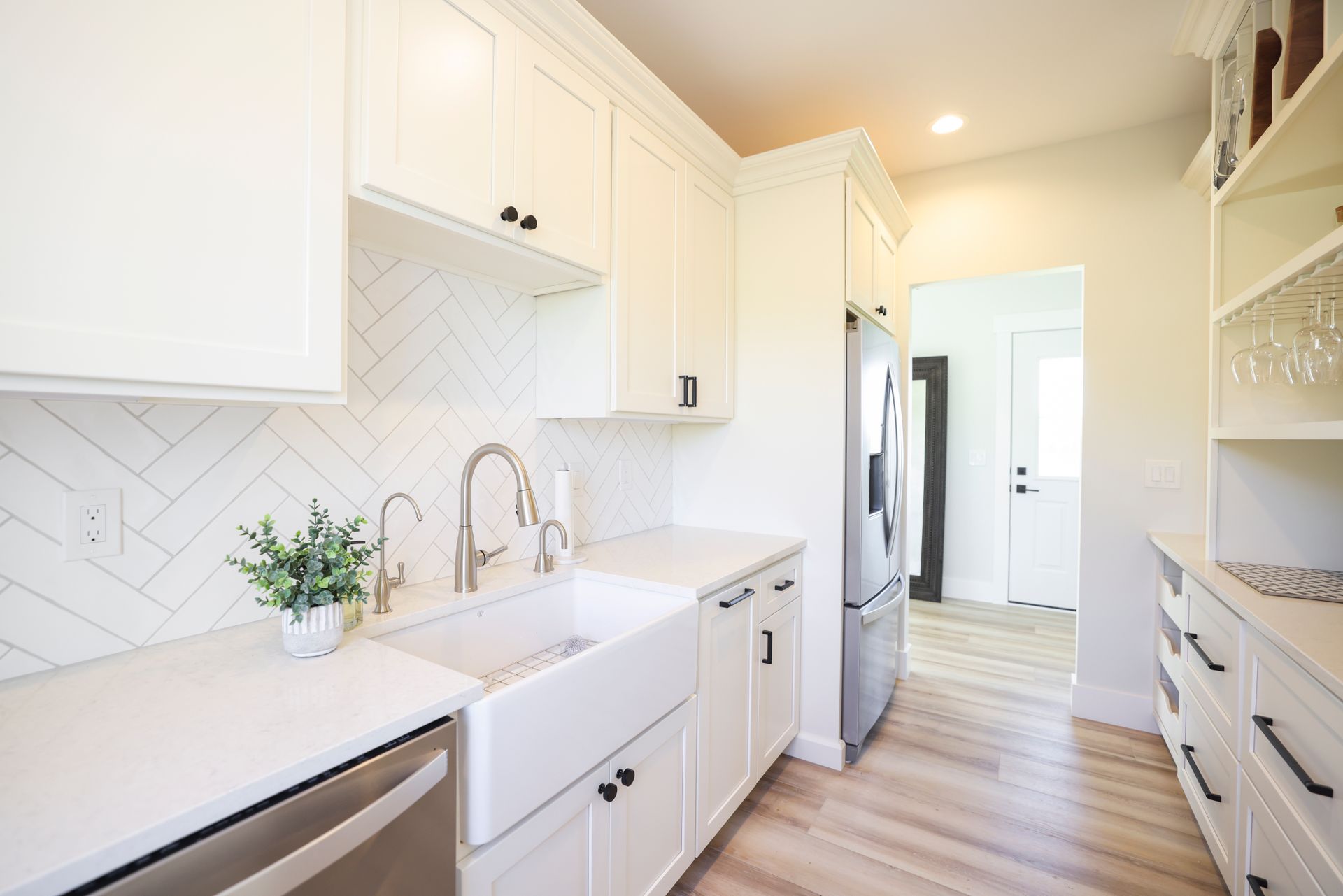 White kitchen with herringbone backsplash, farmhouse sink, stainless steel appliances, and pantry.