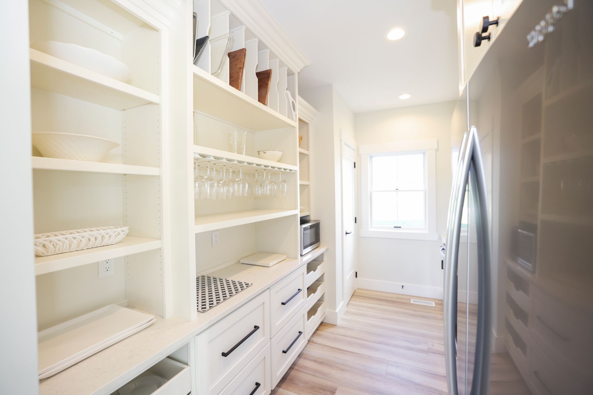 White pantry with built-in shelves and drawers. Light wood floor. Refrigerator on the right.