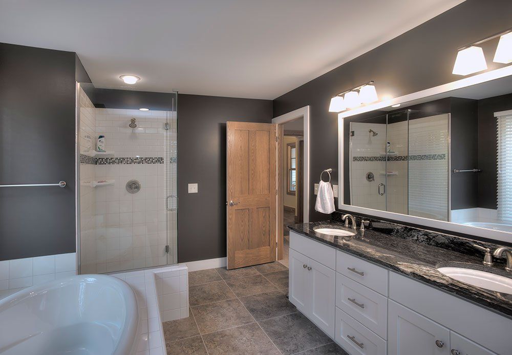 Modern bathroom with gray walls, white cabinets, glass shower, and freestanding tub.