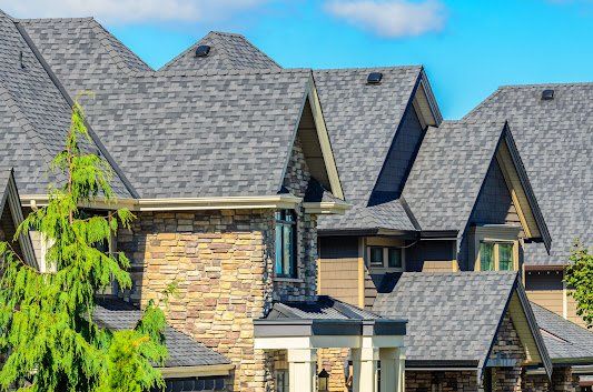 House with multiple gabled roof sections, stone and brown siding, blue sky.