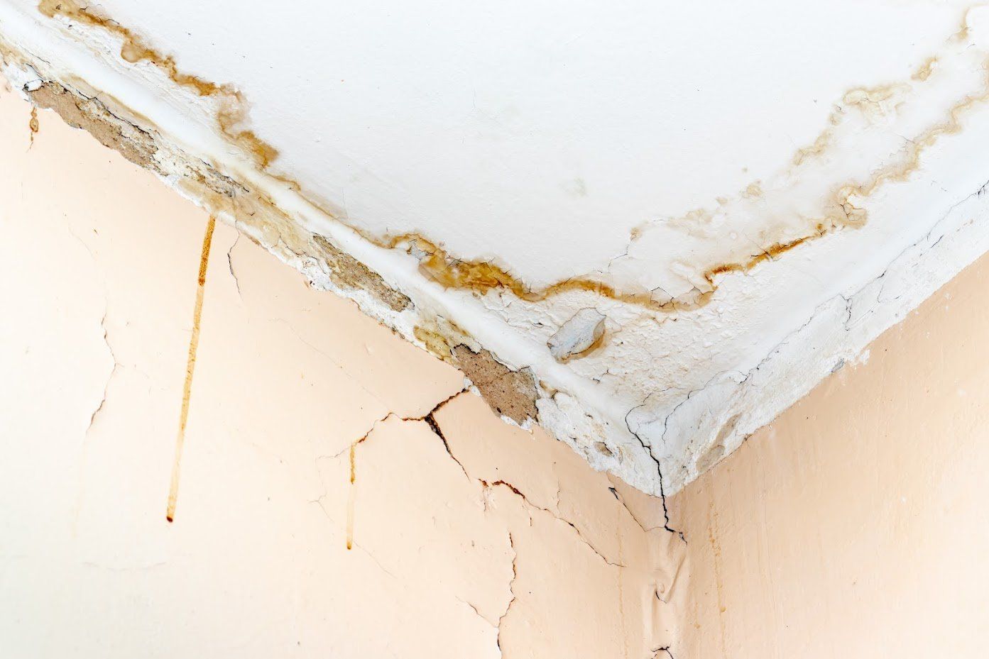 Water damage on ceiling corner with stains and cracks on the wall below.