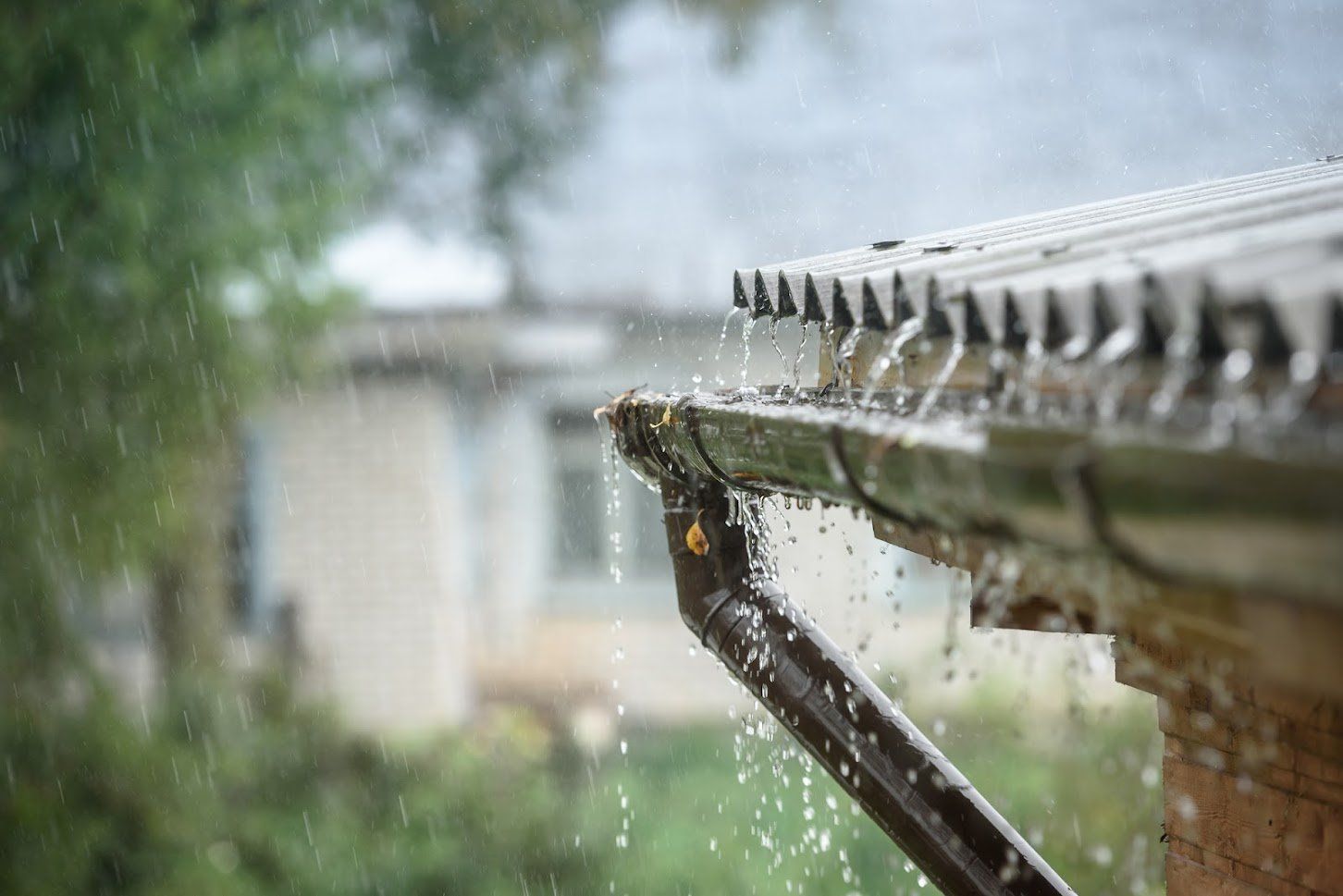 Rainwater pouring from a gutter into a downspout on a house, in a blurred, outdoor setting.