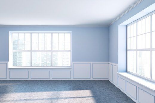 Empty room with blue walls, white trim, two large windows, and sunlight.