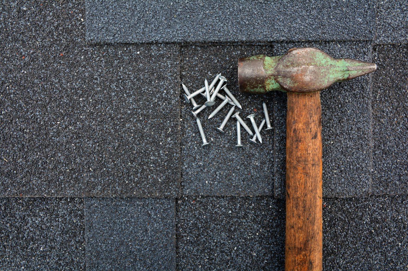 Hammer and nails on gray asphalt shingles.