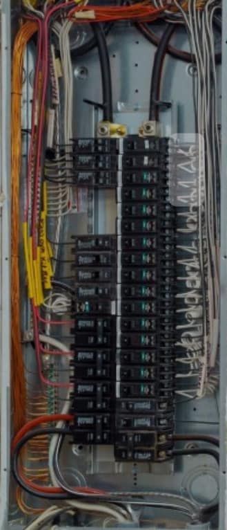 An open electrical panel with two rows of black circuit breakers, various colored wiring, and metal bus bars.