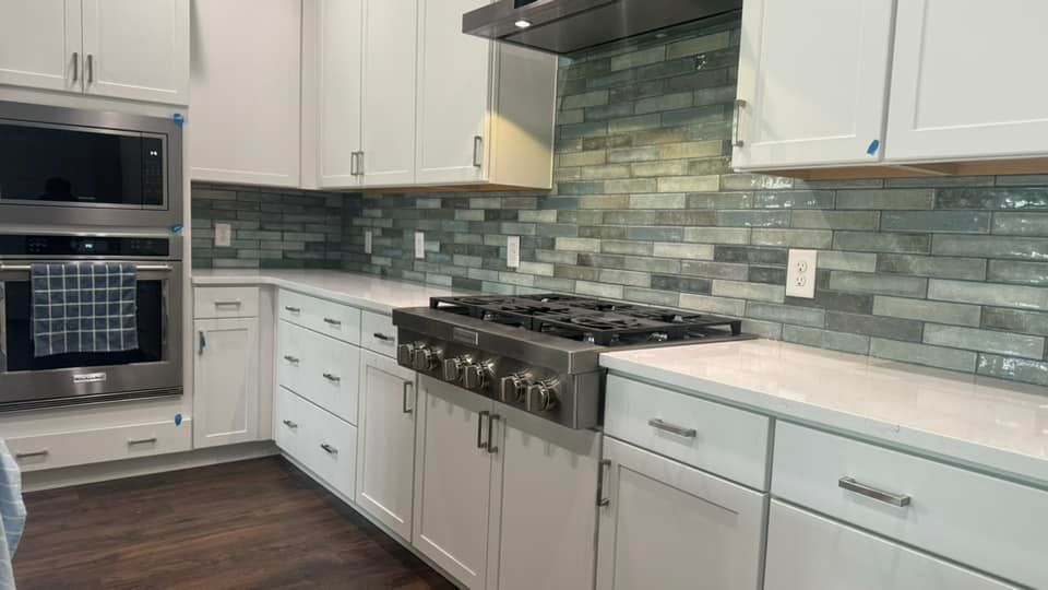 A white kitchen with a stainless steel stove and oven, complemented by a long, blue-toned tile backsplash.