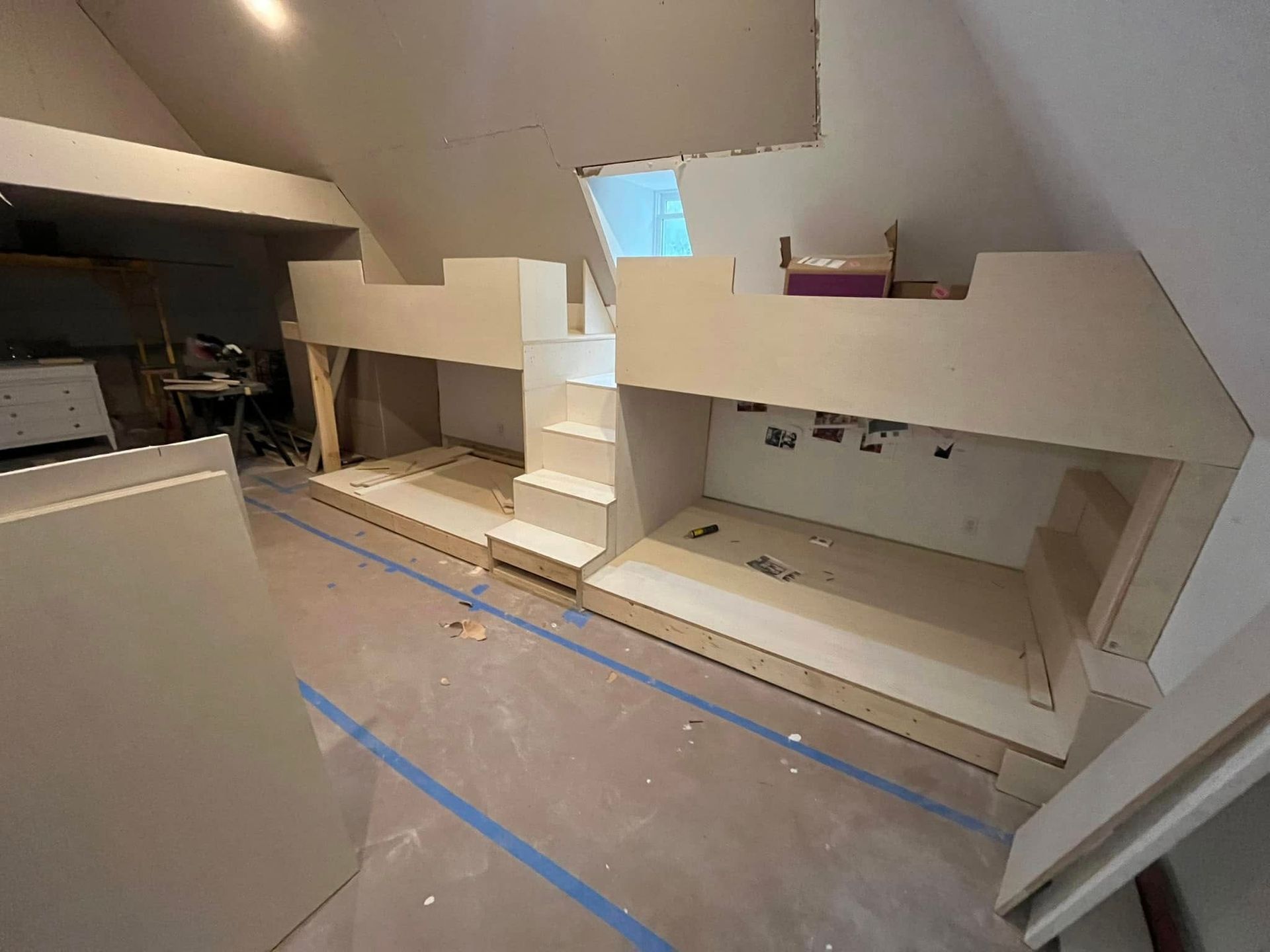 Custom-built bunk beds under construction in a room with slanted ceilings, featuring light-colored wooden framing.