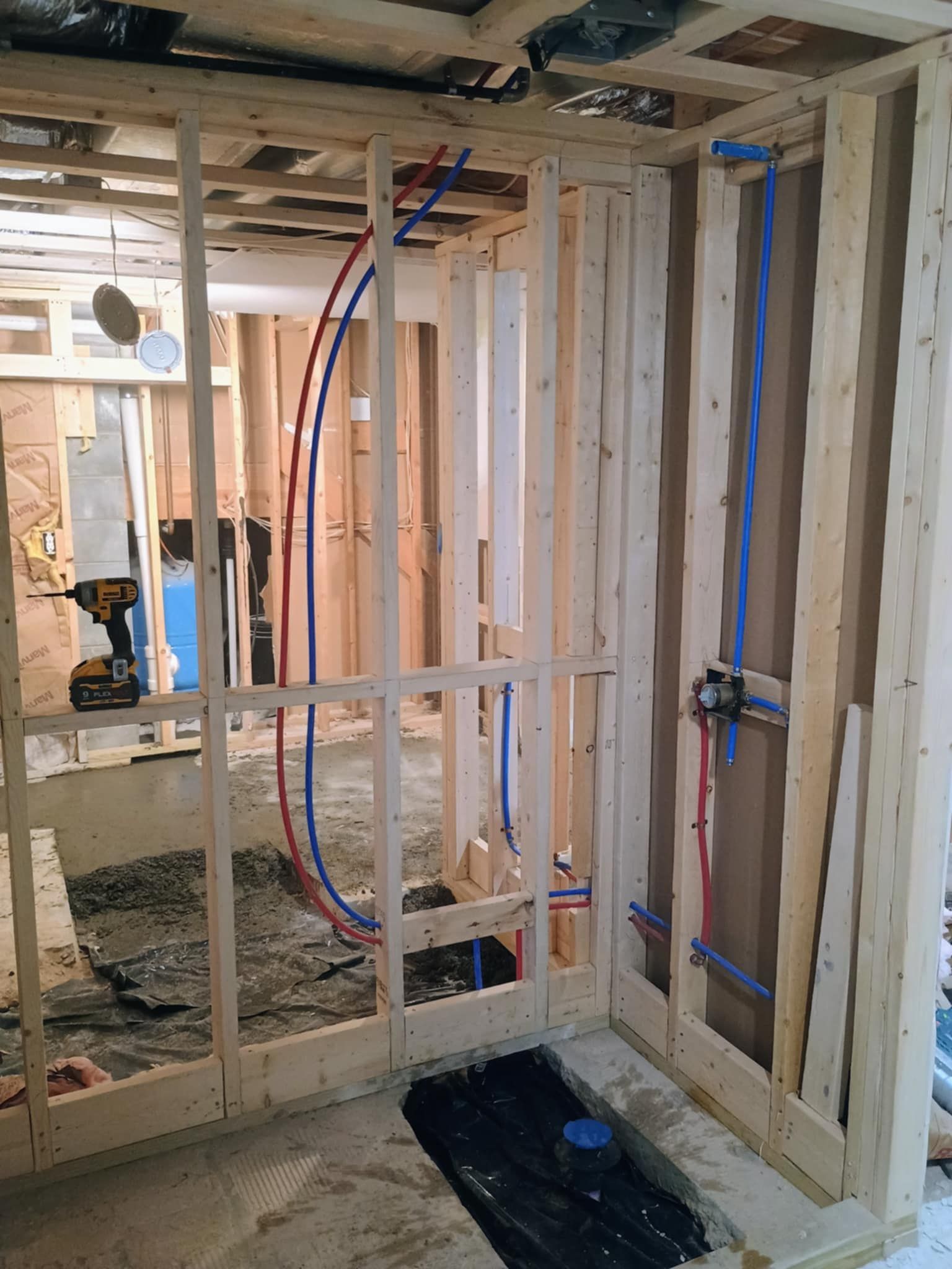 An interior construction project showing exposed wooden wall studs with red and blue PEX plumbing pipes installed.
