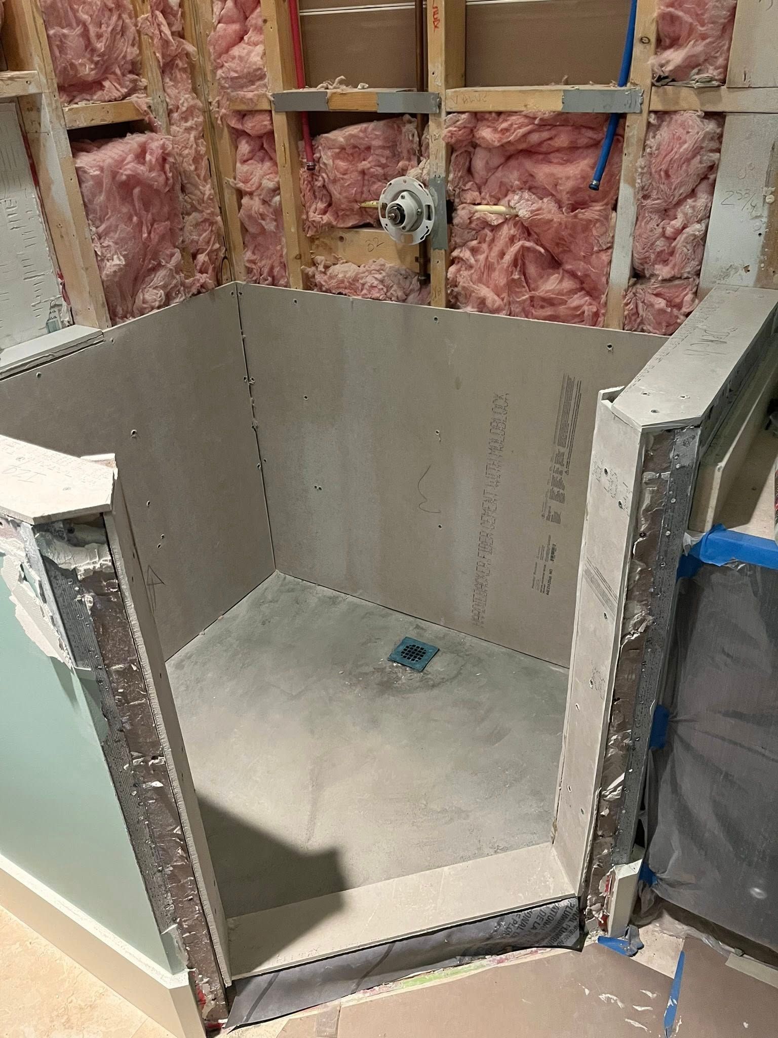A newly installed shower base and backer board walls framed with wood studs and pink insulation in an unfinished room.