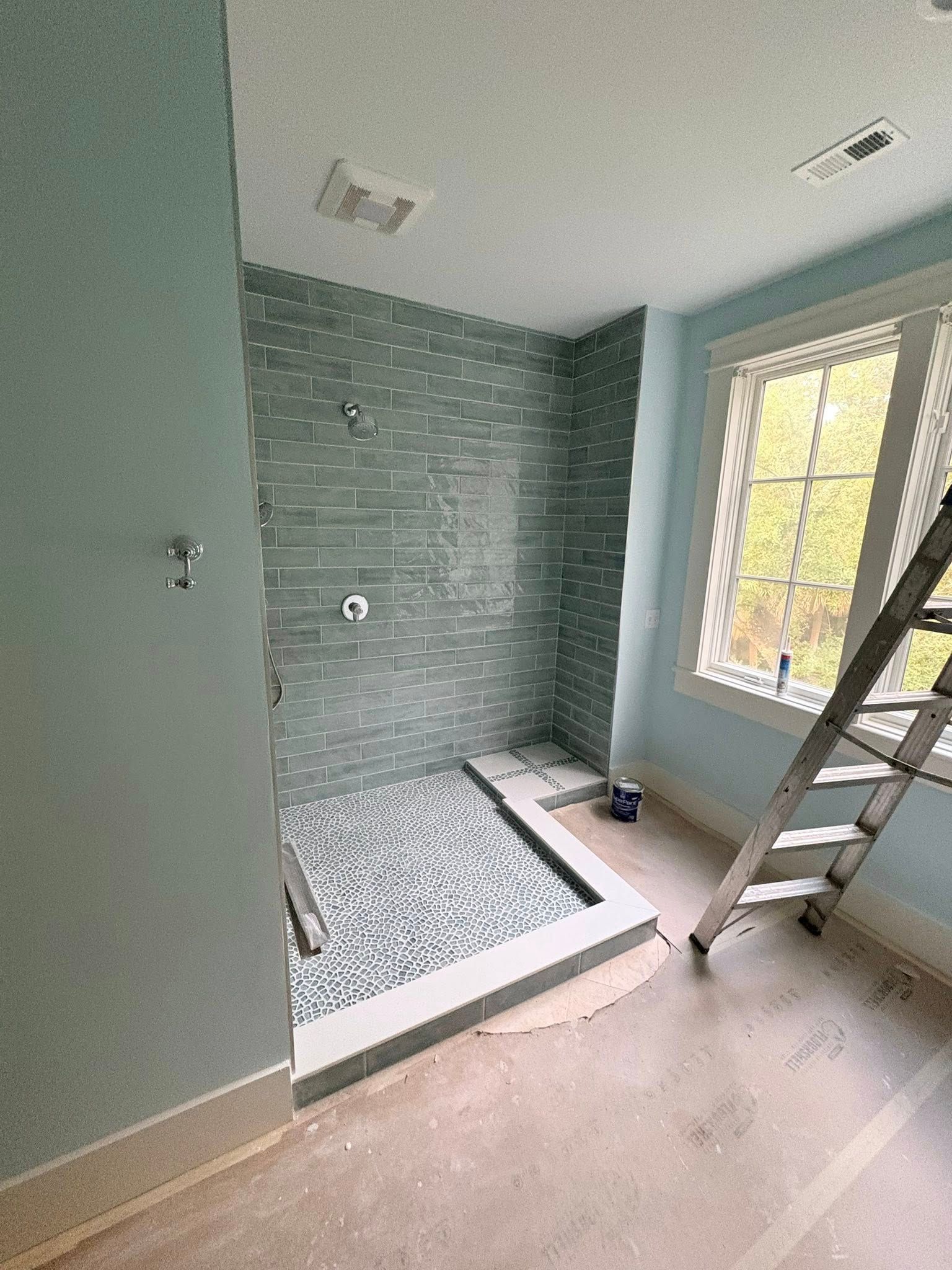 A bathroom under construction featuring a tiled walk-in shower with green subway tile and a pebbled floor.