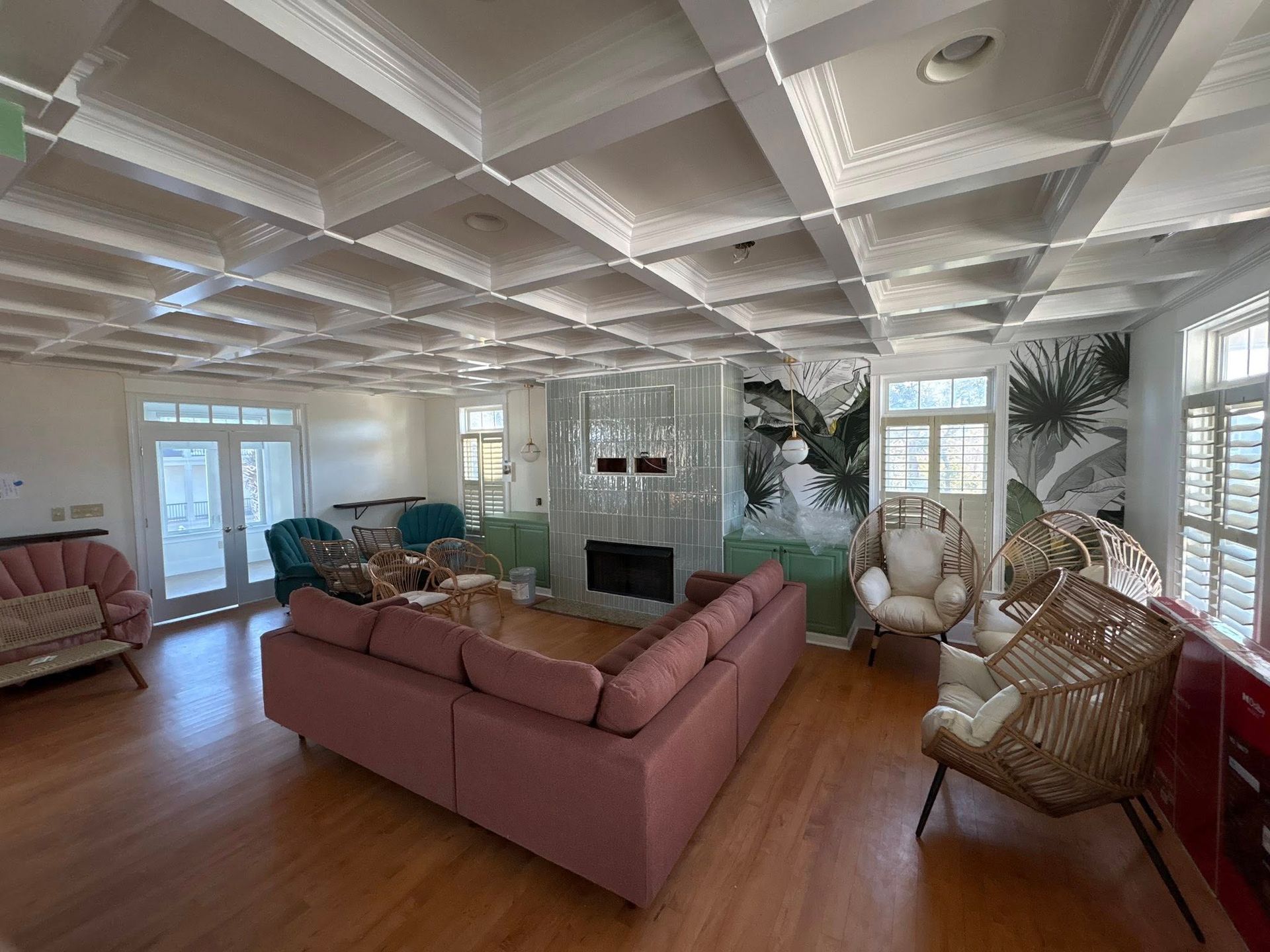 A spacious living room featuring a pink sectional sofa, various chairs, and a unique coffered ceiling with a fireplace.