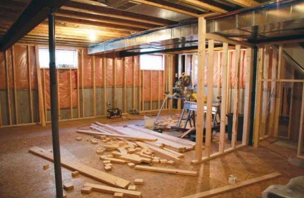 An unfinished basement interior with exposed wooden wall studs, insulation, ceiling joists, and construction debris.