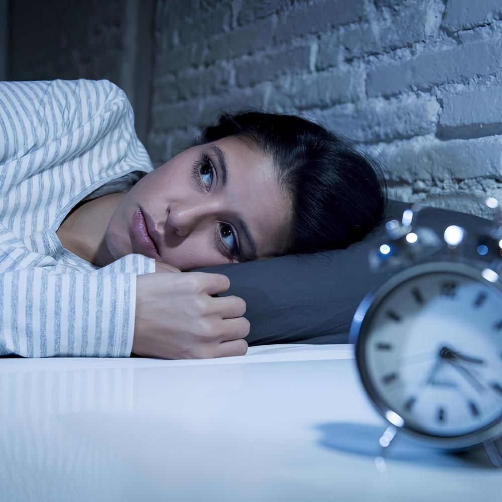Woman lying in bed, awake, looking at a clock. Pale blue and white striped pajamas, dim setting.