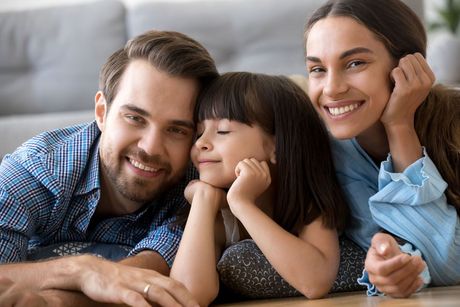 Family of three, smiling, lying on floor together.