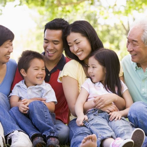 Smiling multi-generational family sitting outdoors; sunny day.