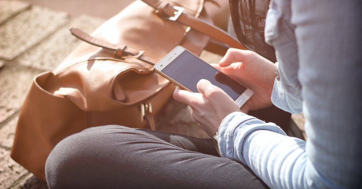Woman holding smartphone; brown bag beside her.