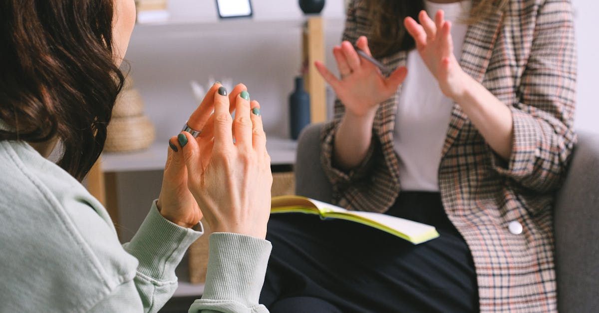 Two women gesturing, one with hands raised, seated, possibly in therapy or discussion.