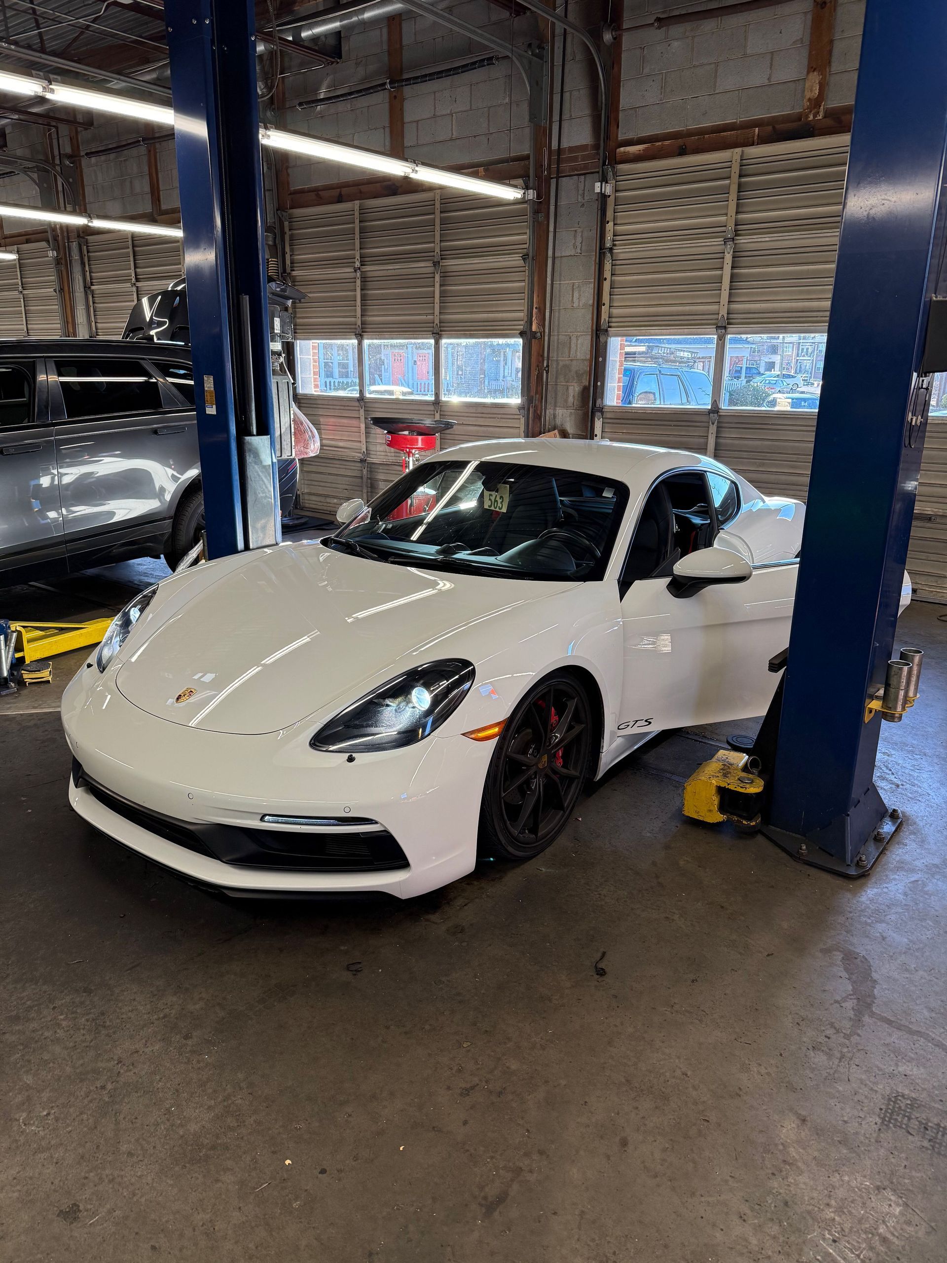 White sports car in a garage bay, parked between lifts with a blue support post in front | Classic Import Auto Service