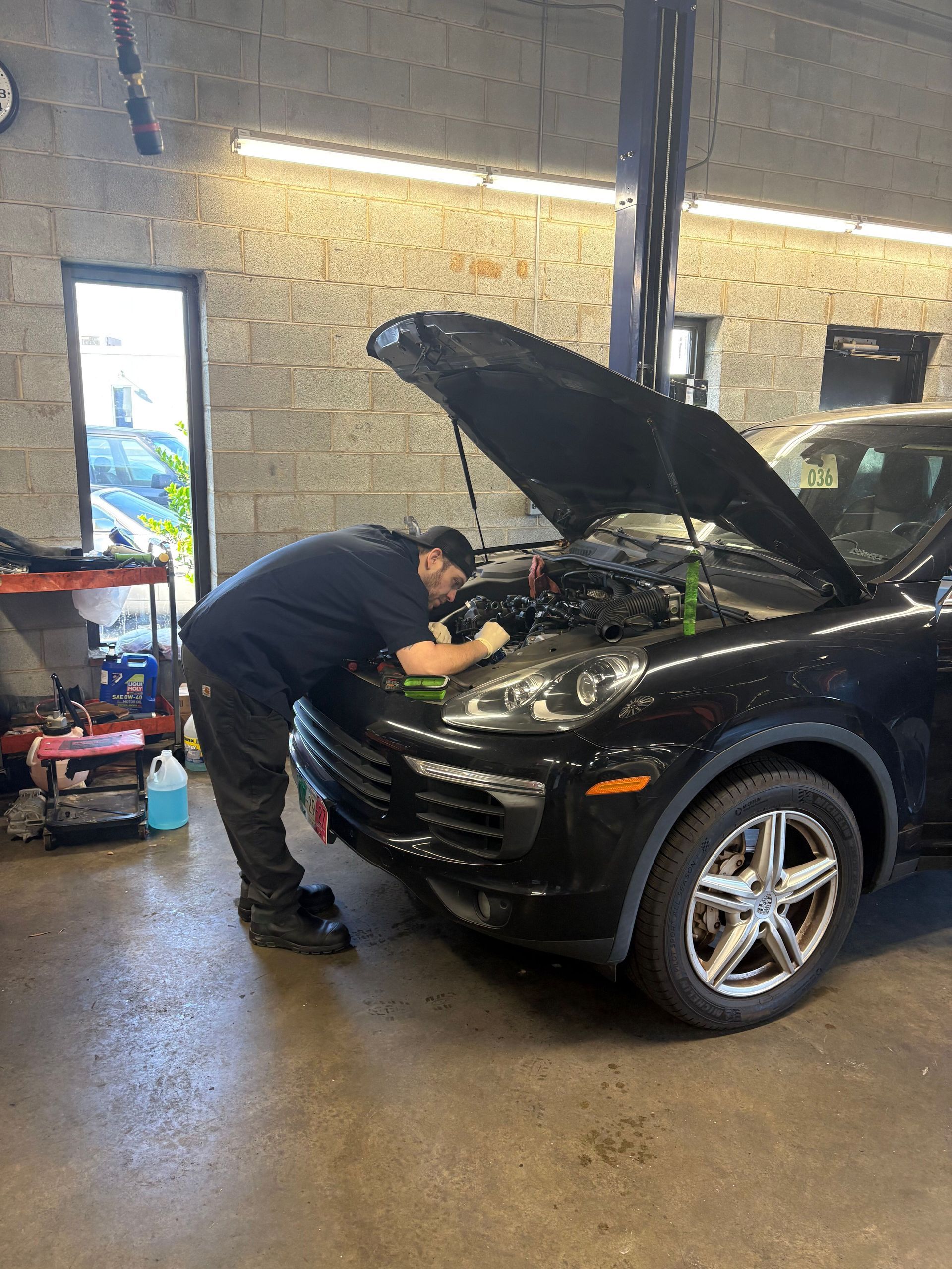 Mechanic working under the hood of a black SUV in an auto repair garage