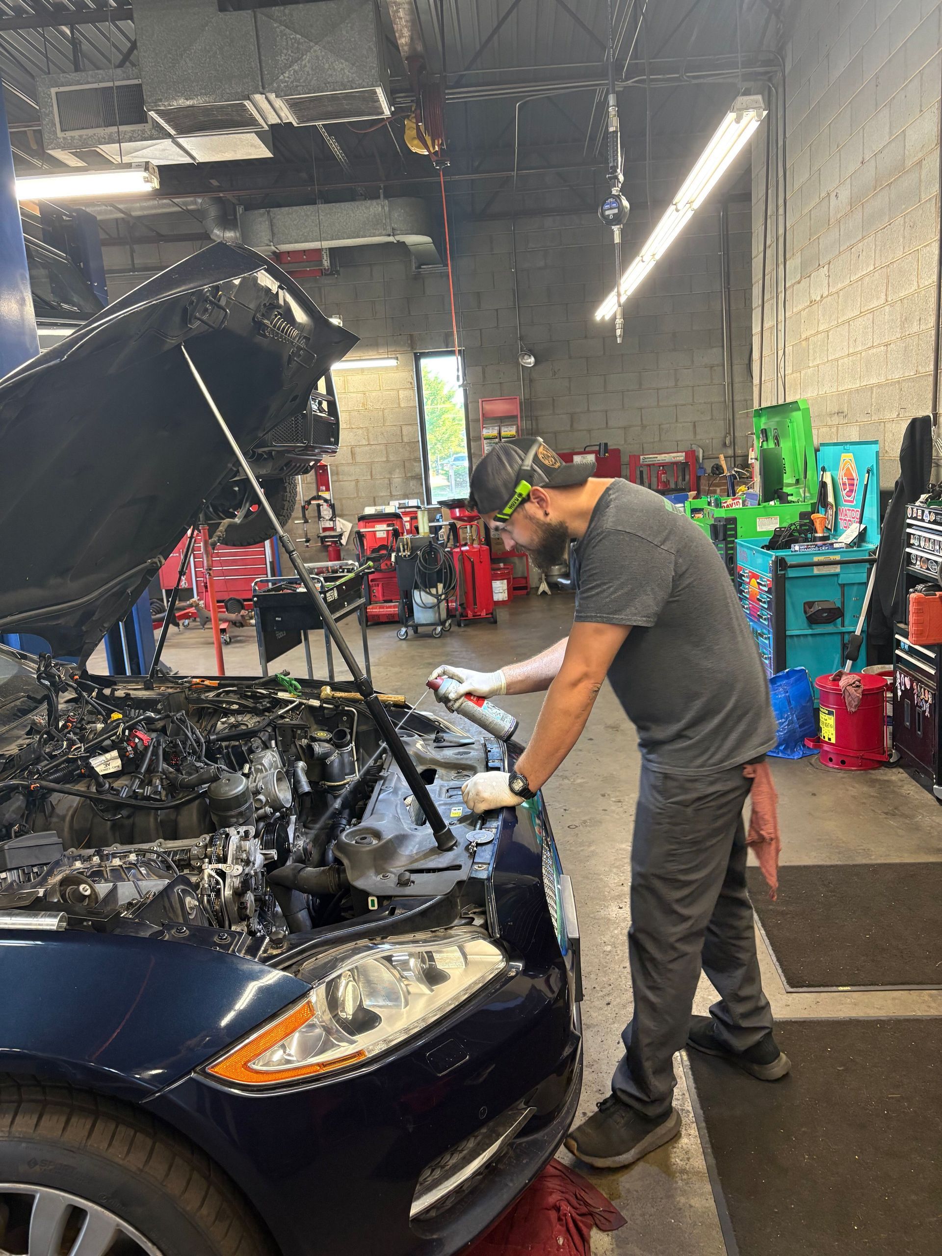 Mechanic in a garage inspects a car with its hood open under bright shop lights | Classic Import Auto Service
