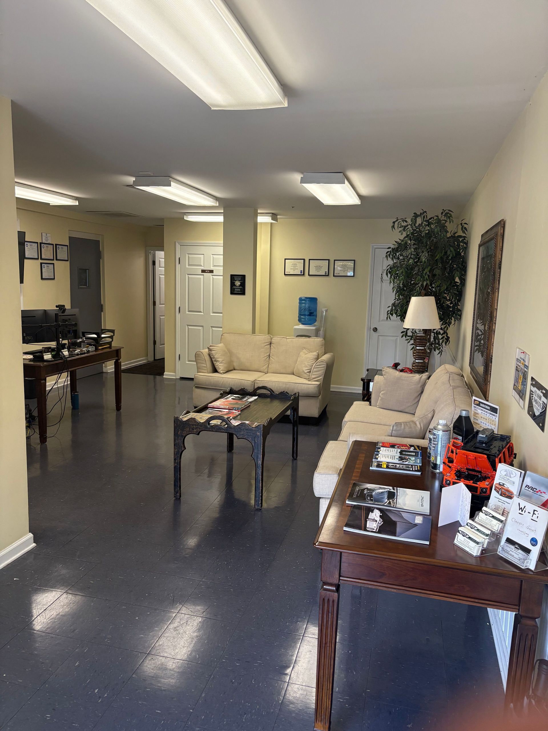 Waiting area with beige couches, coffee tables, fluorescent lights, and framed wall decor in an office lobby | Classic Import Auto Service