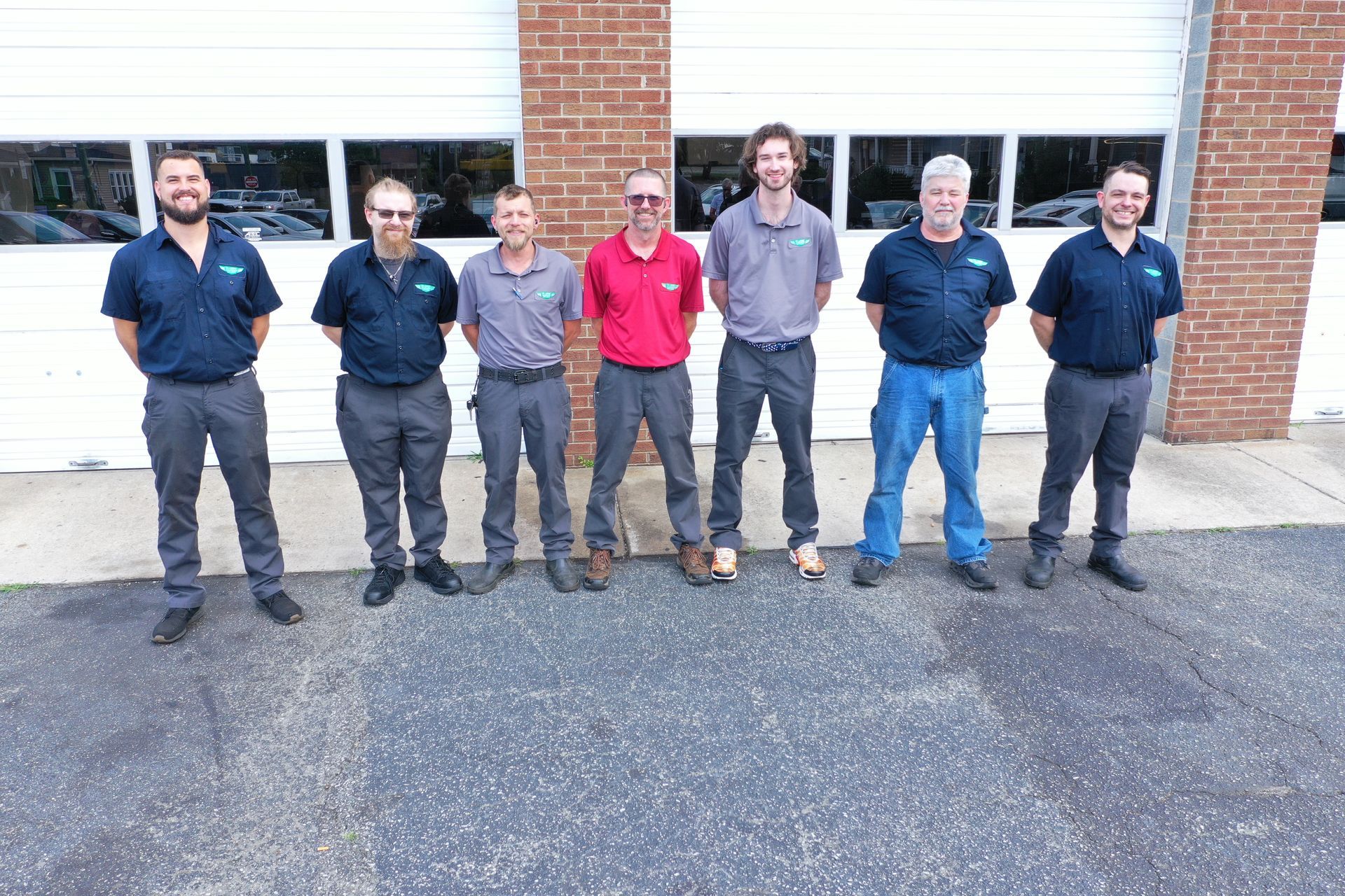 Six people standing outdoors in front of a white garage door and brick wall, wearing casual work clothes | Classic Import Auto Service