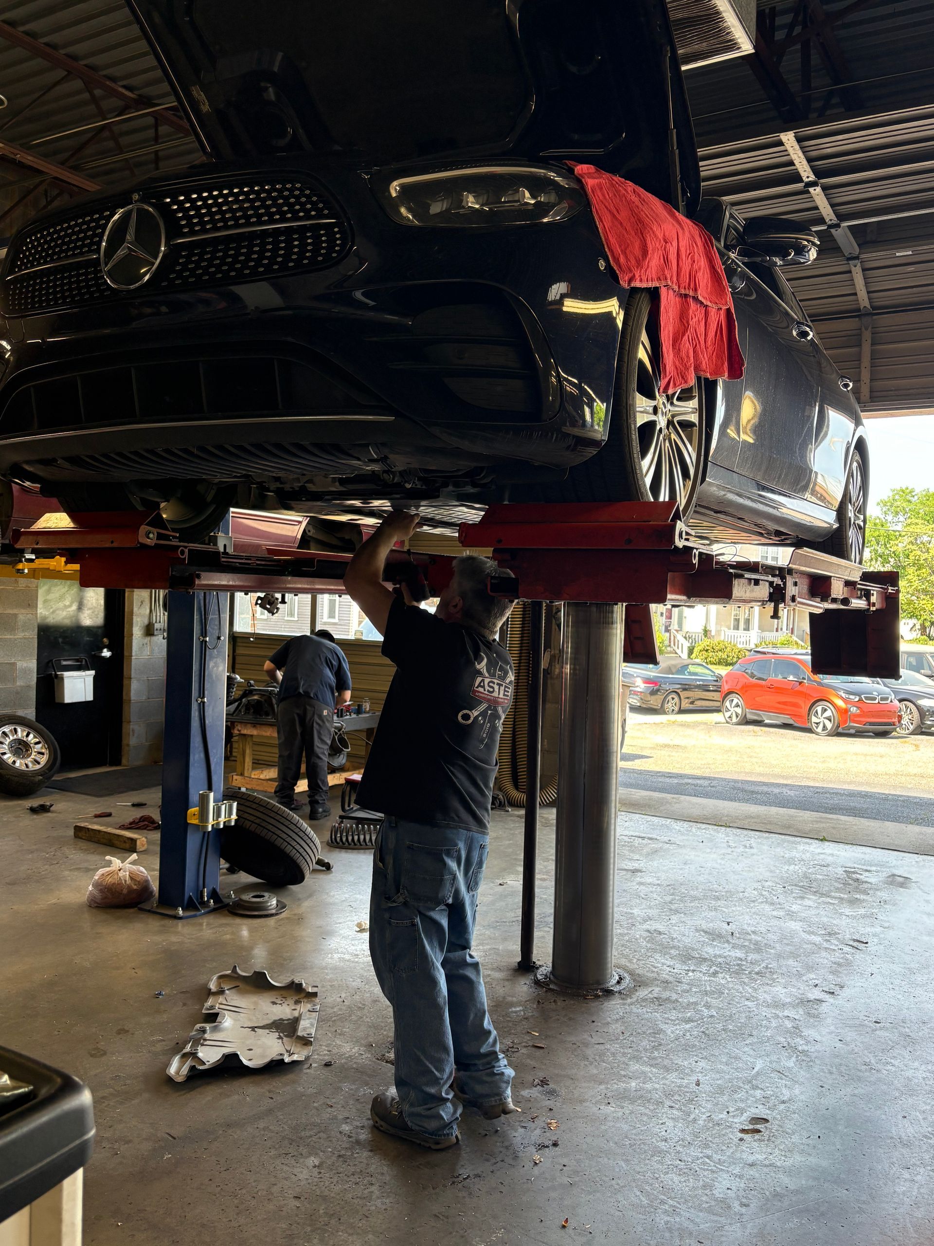 Mechanic working under a raised black vehicle in an auto repair shop | Classic Import Auto Service