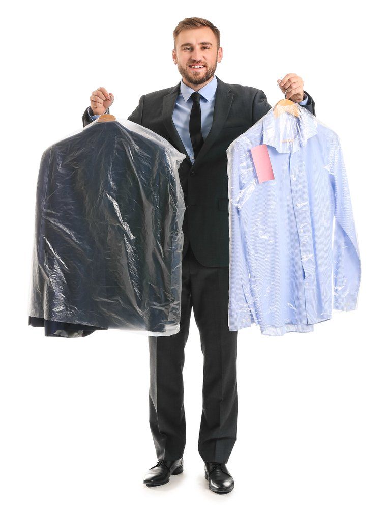 Un homme en costume tenant une veste et une chemise fraîchement nettoyées dans une pellicule plastique.
