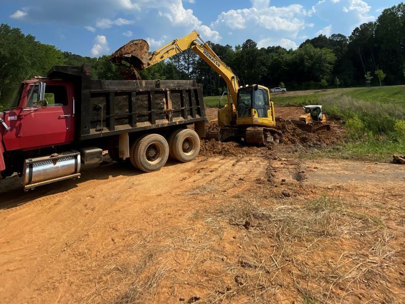 A yellow excavator is loading dirt into a dump truck