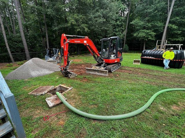 A man is standing next to a small excavator in a yard.